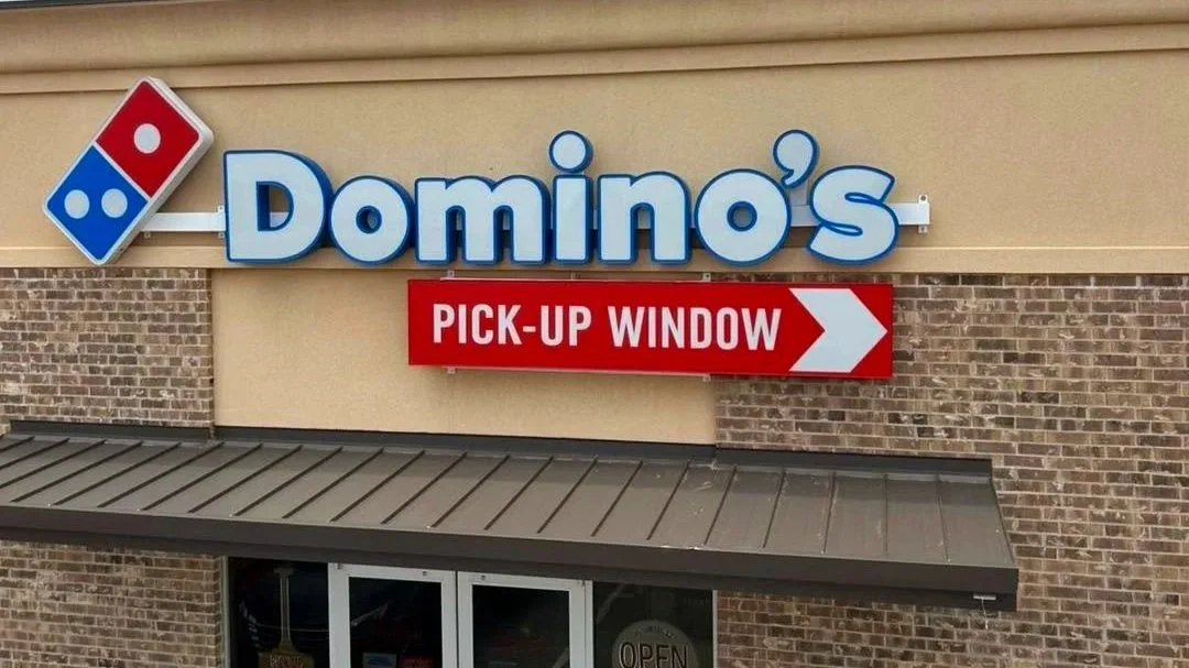 Domino's Pizza storefront with sign indicating a pickup window marked with a red rectangular sign and white arrow.