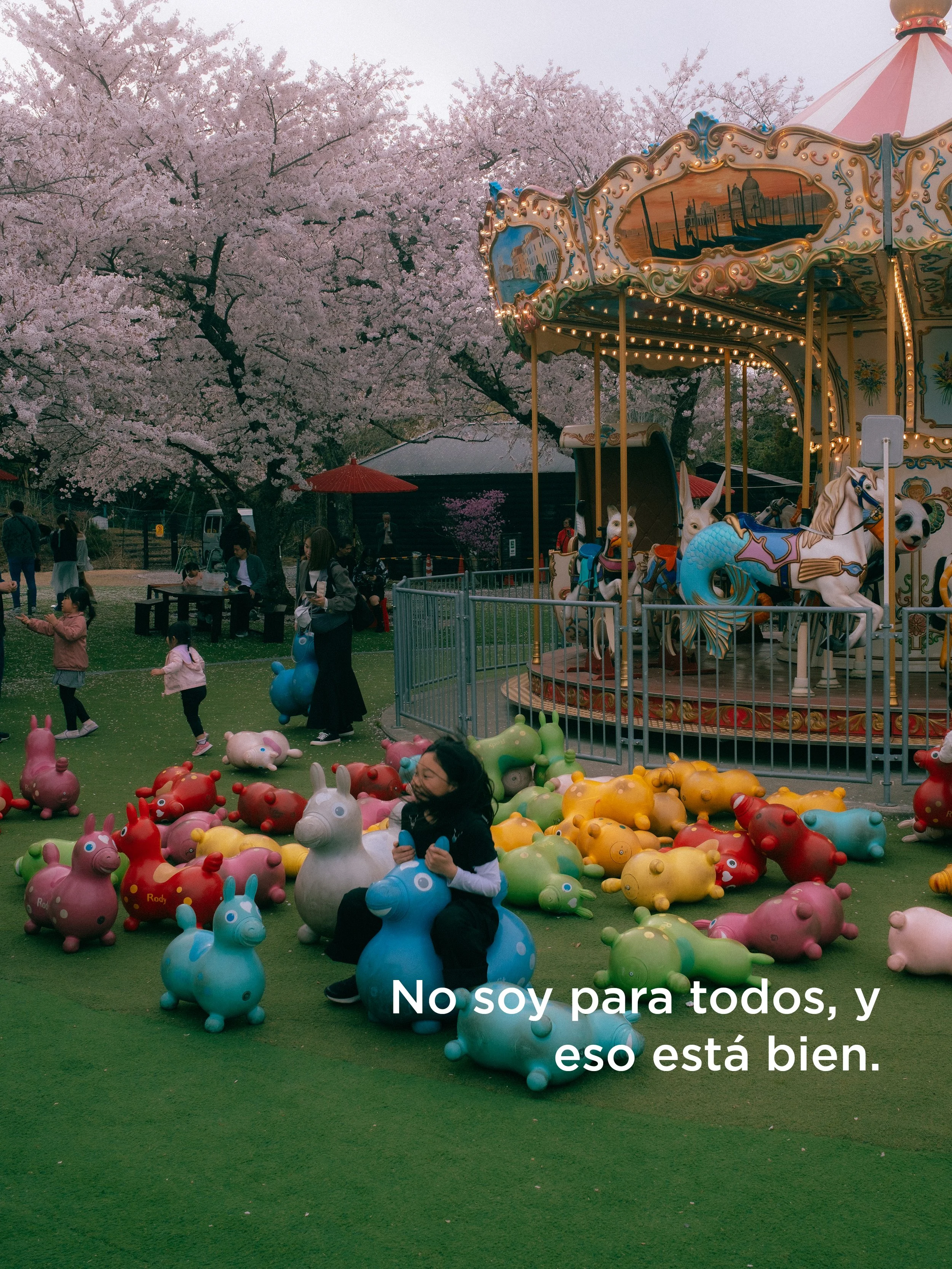 Niños jugando con ovejitas de plástico en un parque con un carrusel en el fondo, árboles en flor y un cielo nublado, con texto en la parte inferior que dice 'No soy para todos, y eso está bien.'