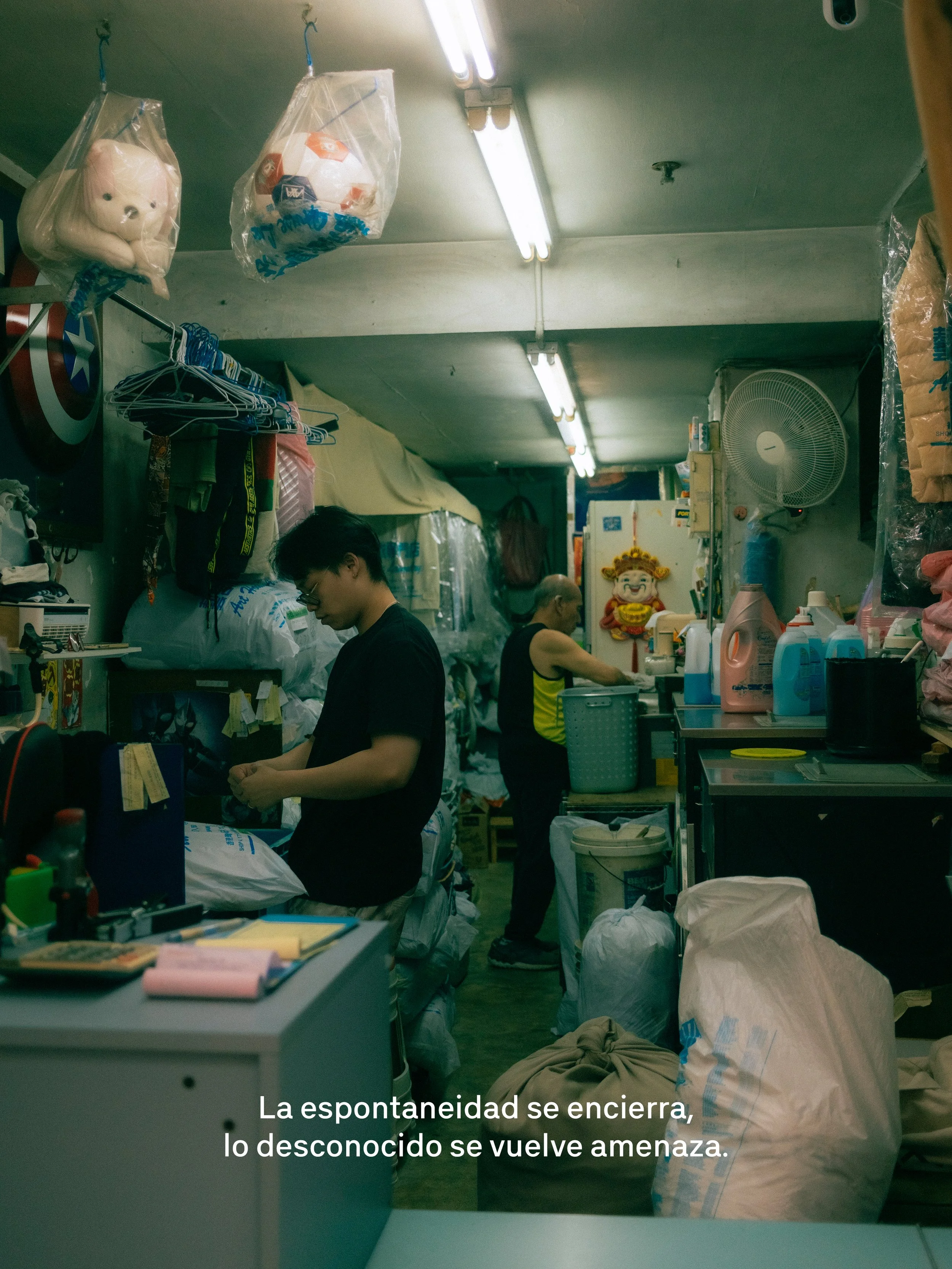 Personas en un espacio cerrado rodeadas de bolsas llenas y objetos diversos, en un ambiente que parece ser un almacén o lavandería.