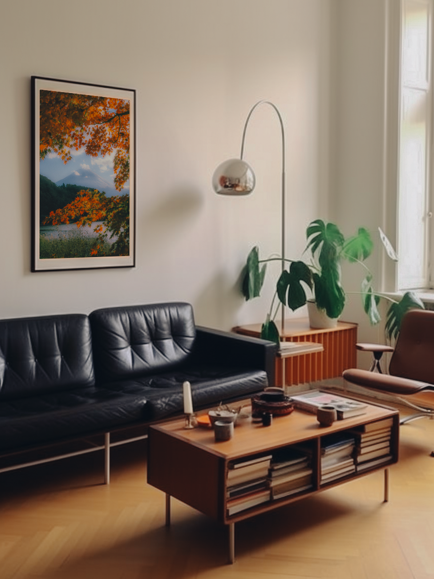 Sala de estar con sillón negro, mesa de madera con revistas y objetos decorativos, planta grande en la esquina y cuadro con paisaje otoñal en la pared.