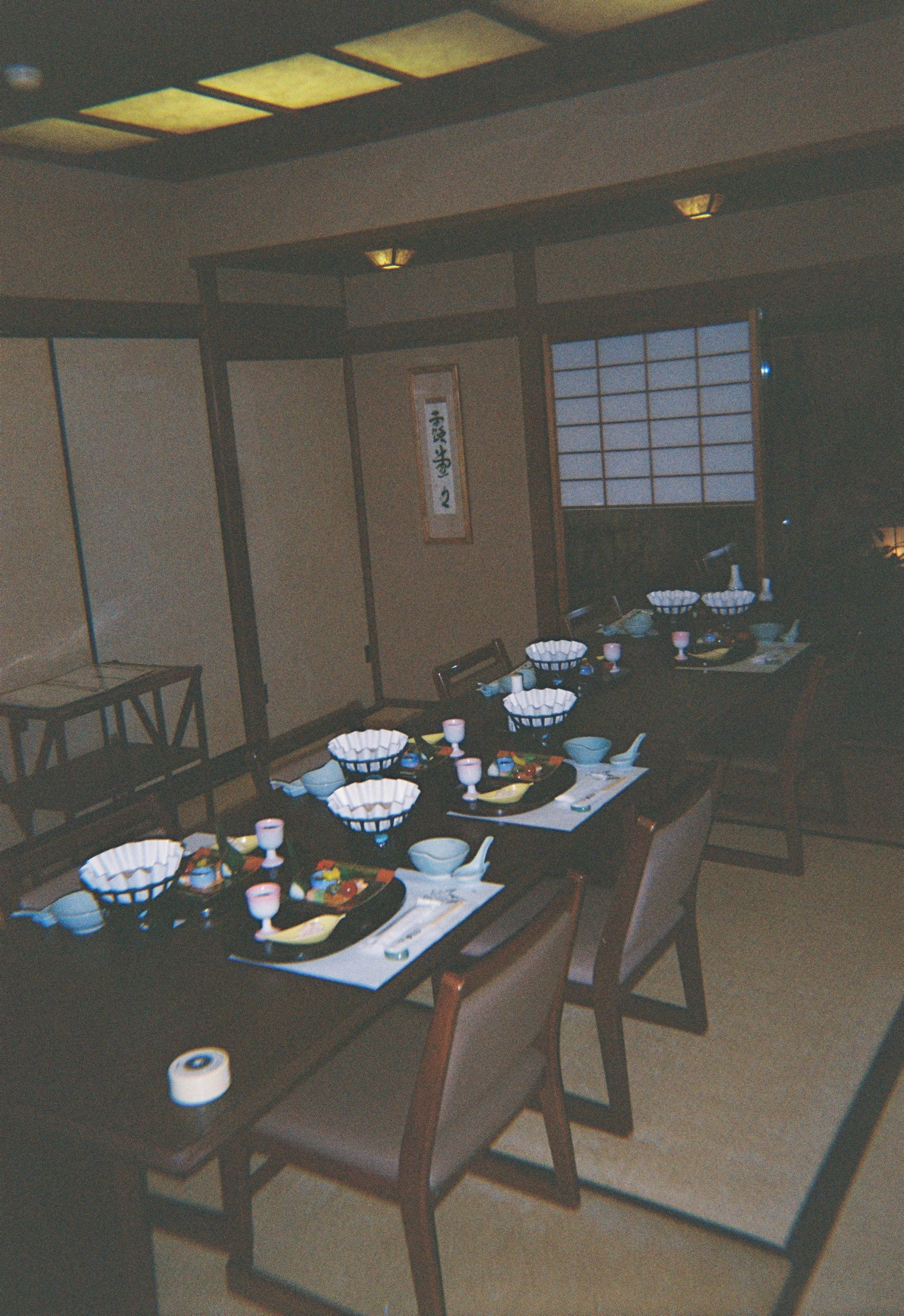 Mesa decorada con platos, tazas y utensilios para comer, en un ambiente de estilo japonés con puertas shoji y decoración sencilla.