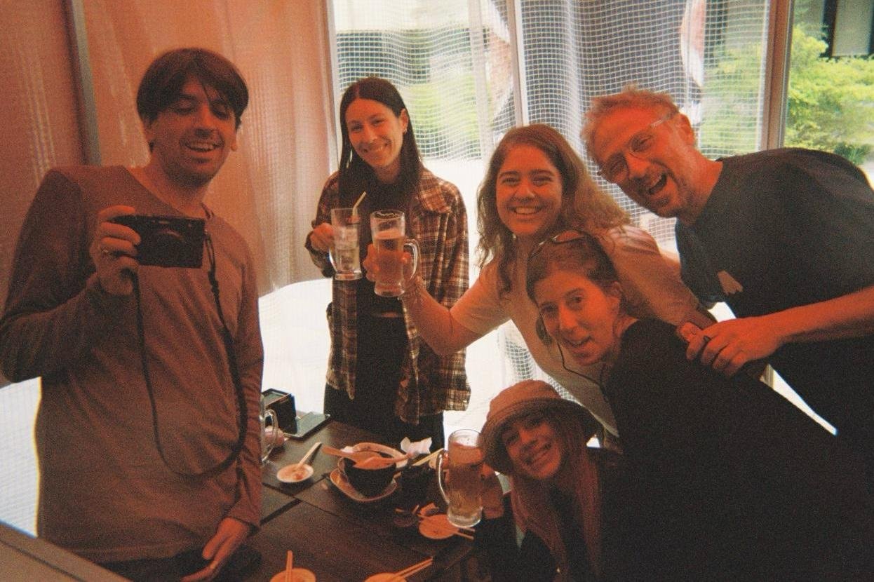 Grupo de seis personas brindando con bebidas en un restaurante durante una celebración en interior con ventanas de fondo