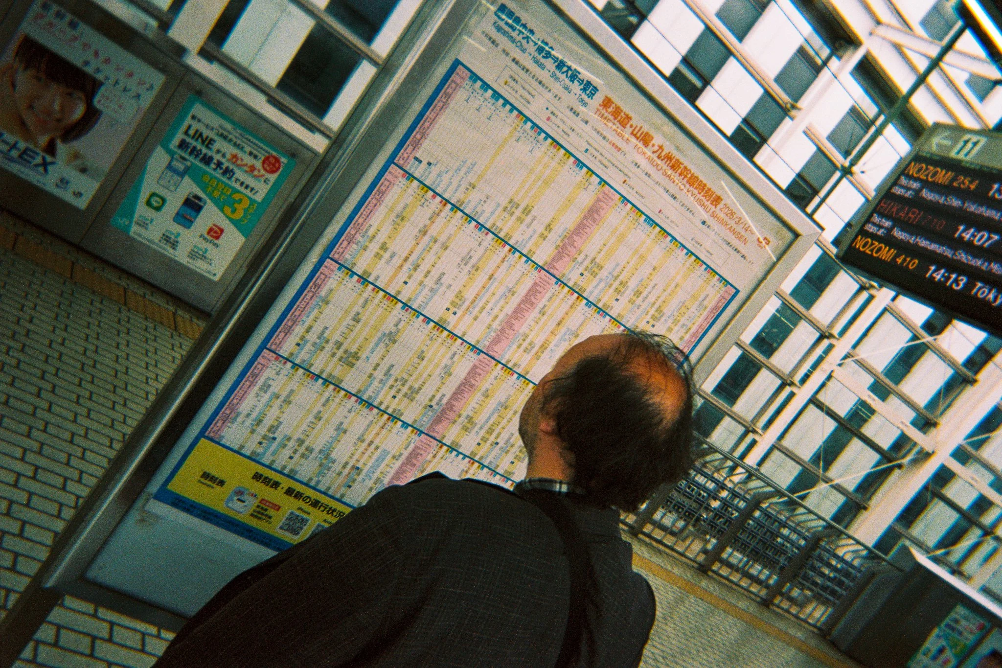 Persona de espaldas mirando un horario de trenes en una estación en Japón, con carteles y pantallas electrónicas