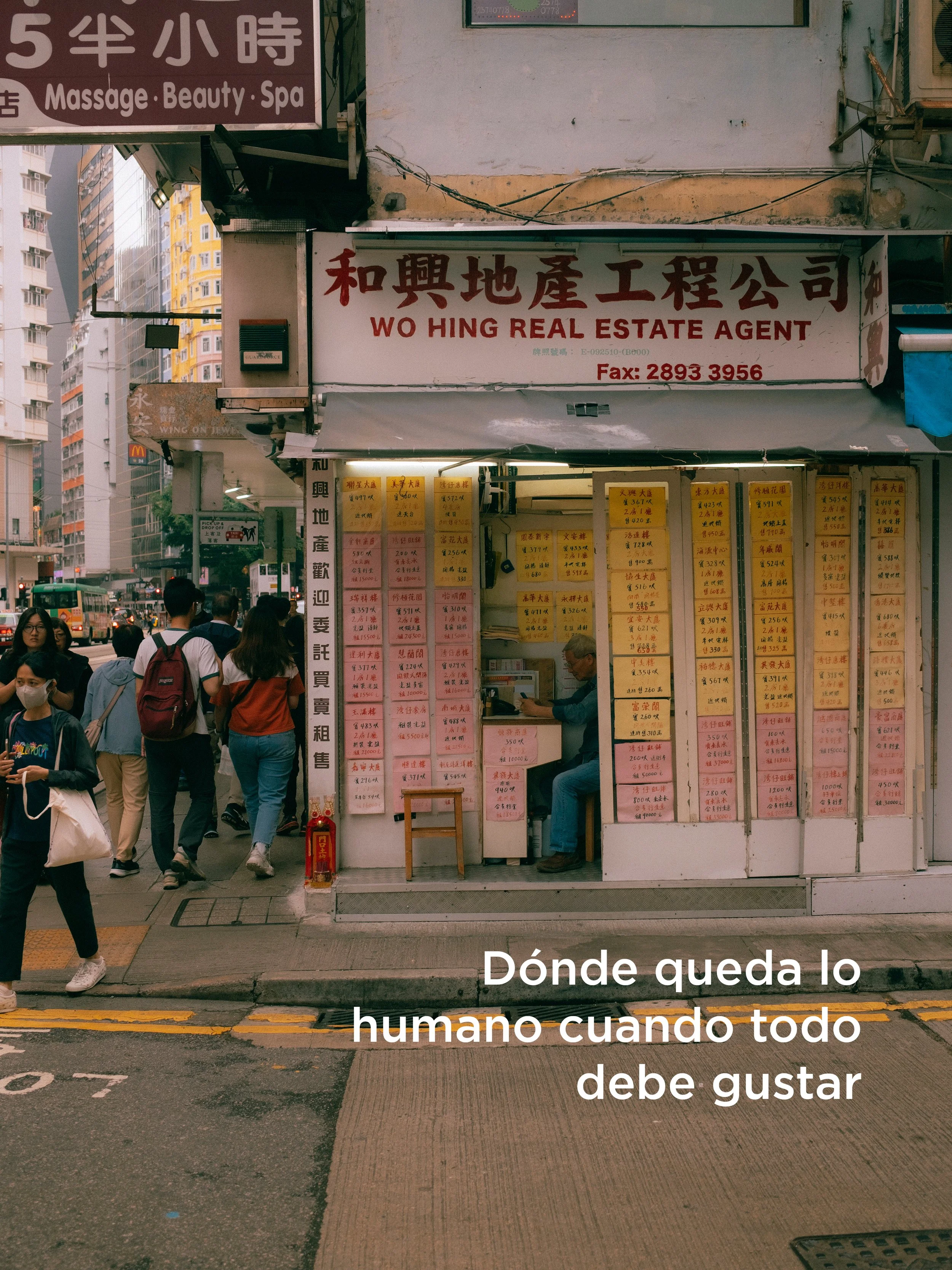 Una parada de venta de boletos con muchas hojas con precios escritos. En la parte superior, un cartel en chino que dice 'WO HING REAL ESTATE AGENT' y una multitud de personas caminando por la acera.