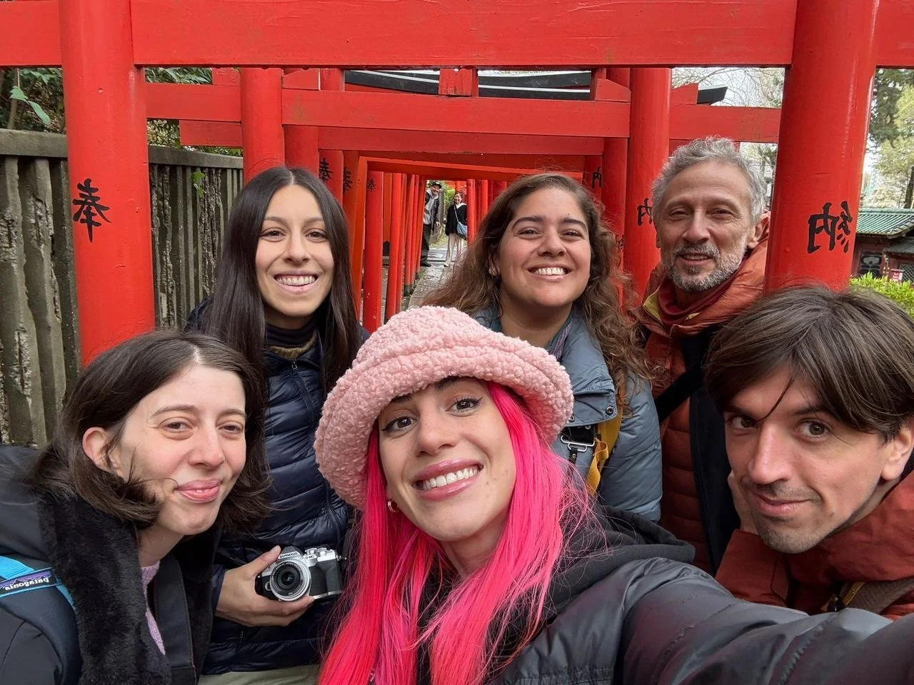 Grupo de seis personas tomando una selfie frente a fila de torii rojos en un santuario japonés