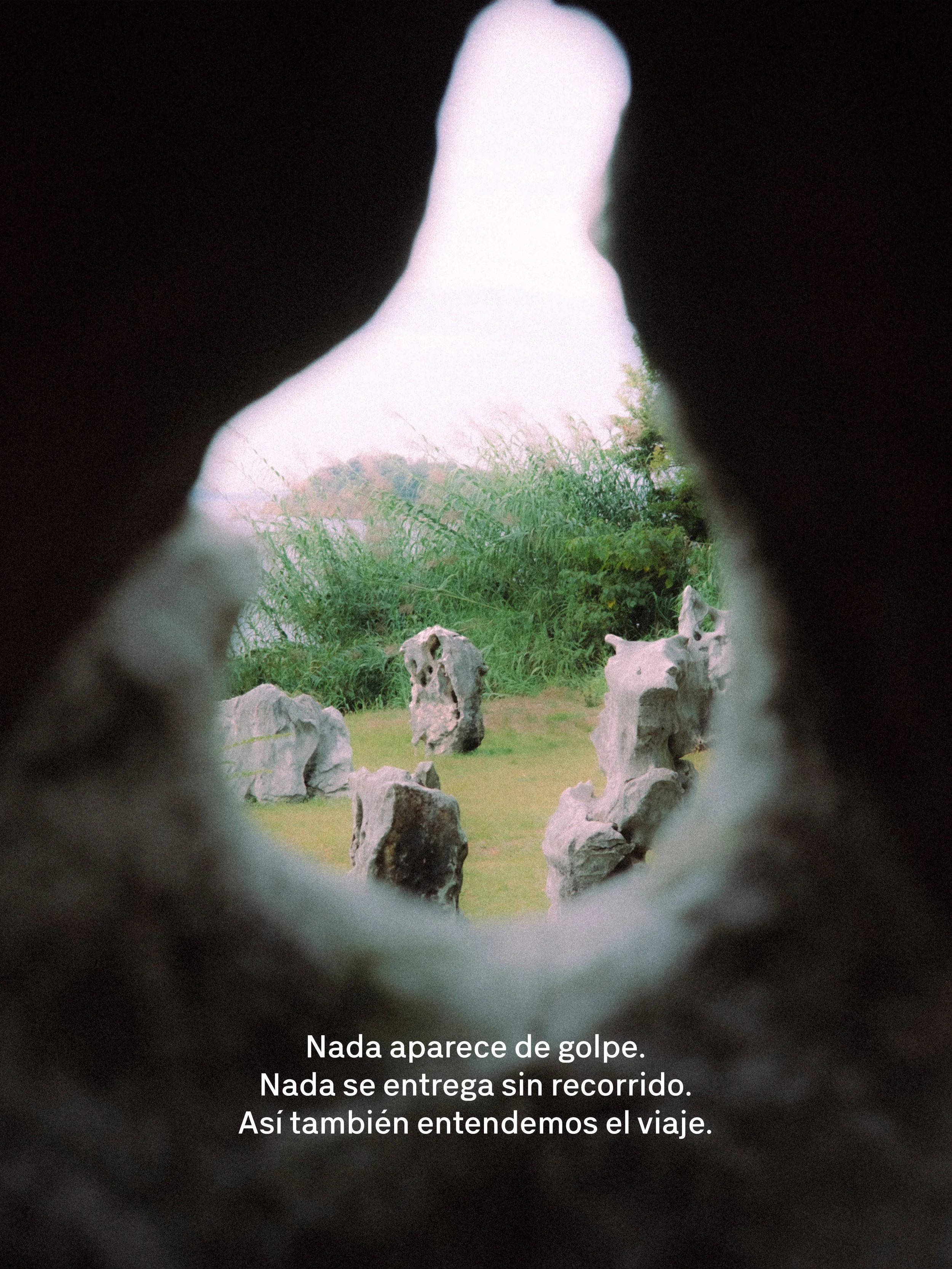Vista a través de un agujero en la pared, con piedras y vegetación, texto en español que dice: "Nada aparece de golpe. Nada se entrega sin recorrido. Así también entendamos el viaje."
