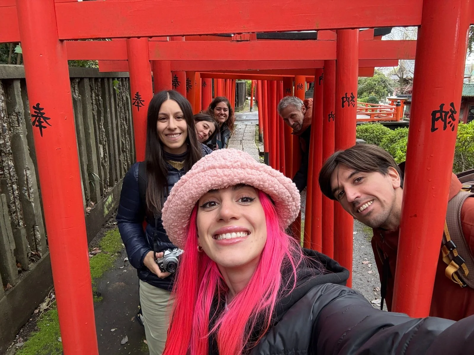 Grupo de seis personas en un pasillo de torii rojos en un templo japonés, sonriendo y tomando una selfie.