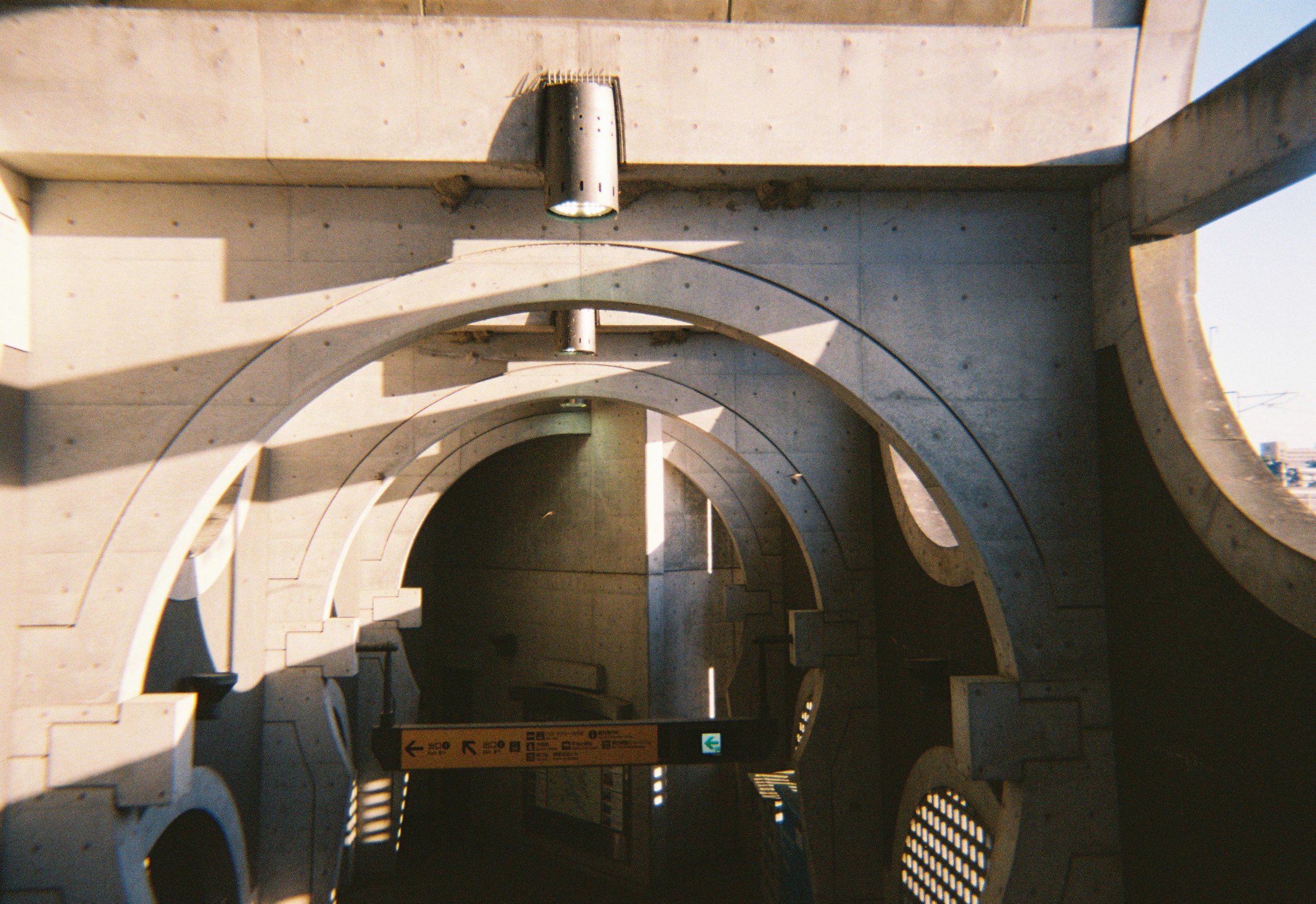 Pasillo de estación de metro con arcos de concreto y señalización en la pared y el suelo, con sombra prolongada en el piso.