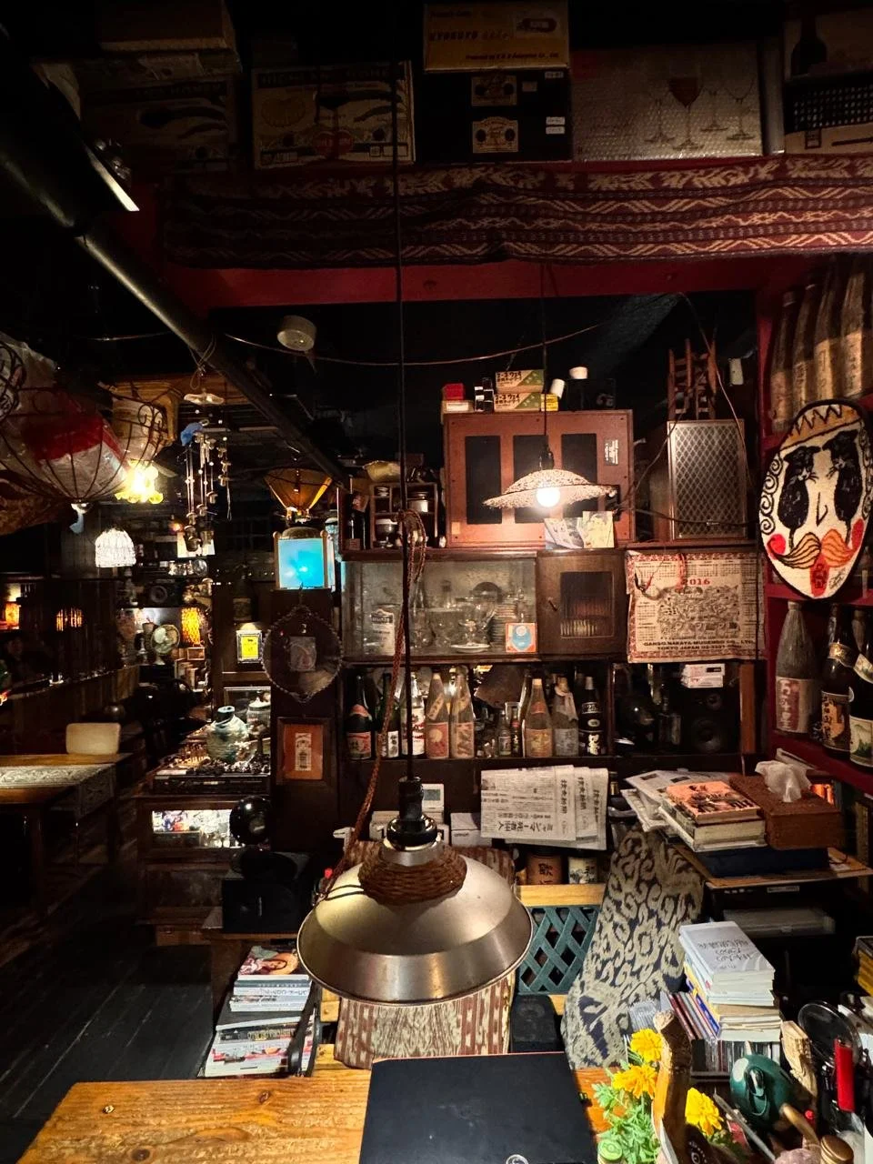 Interior de un restaurante o una cafetería con decoración vintage, estanterías con botellas, libros, y objetos antiguos, y una lámpara colgante en primer plano.