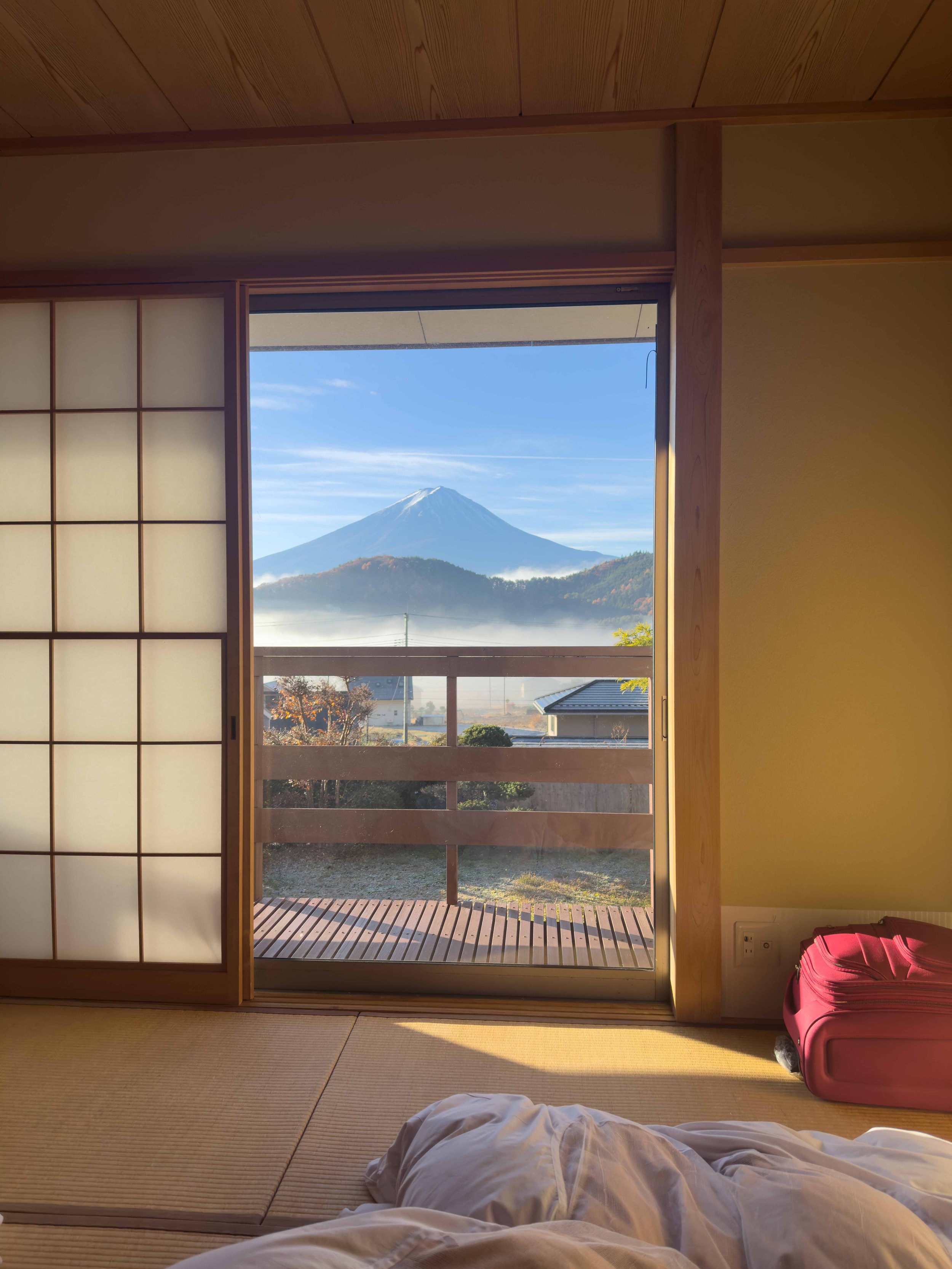 Vista de una habitación con puertas correderas de madera y papel de arroz, mostrando una vista del Monte Fuji y un paisaje con árboles y casas desde un balcón.