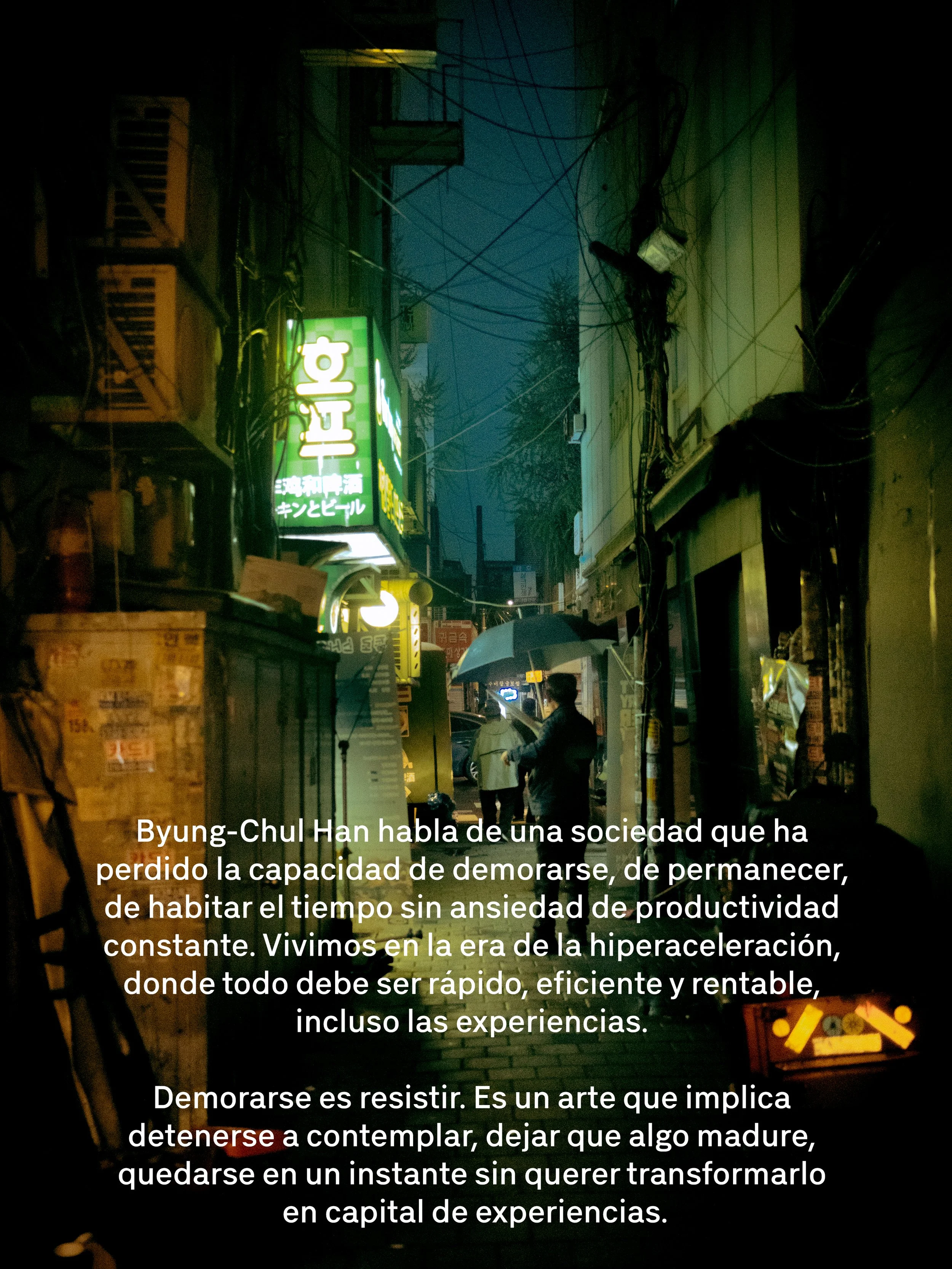 Una calle oscura y lluviosa en la noche con carteles y cables, una persona sostiene un paraguas.