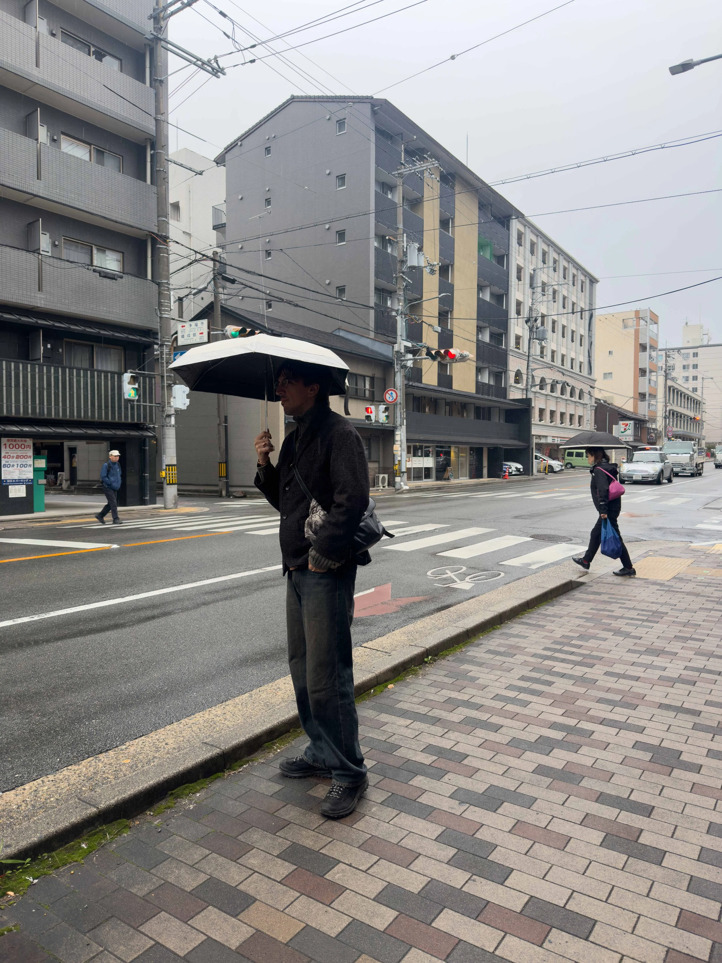 Persona con sombrilla en una calle de ciudad en un día lluvioso, con edificios y tráfico en el fondo.