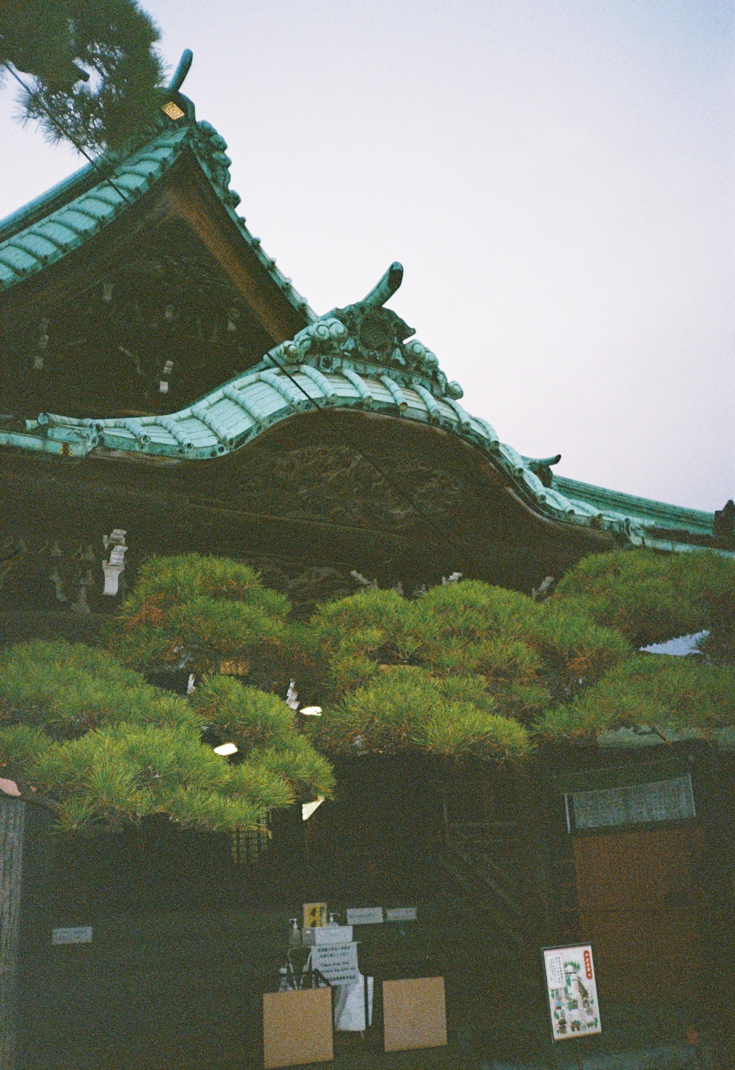 Parte de un techo tradicional japonés con detalles ornamentales en los extremos y en las esquinas, adornado con tejas verdes y decoraciones en formas de dragón.