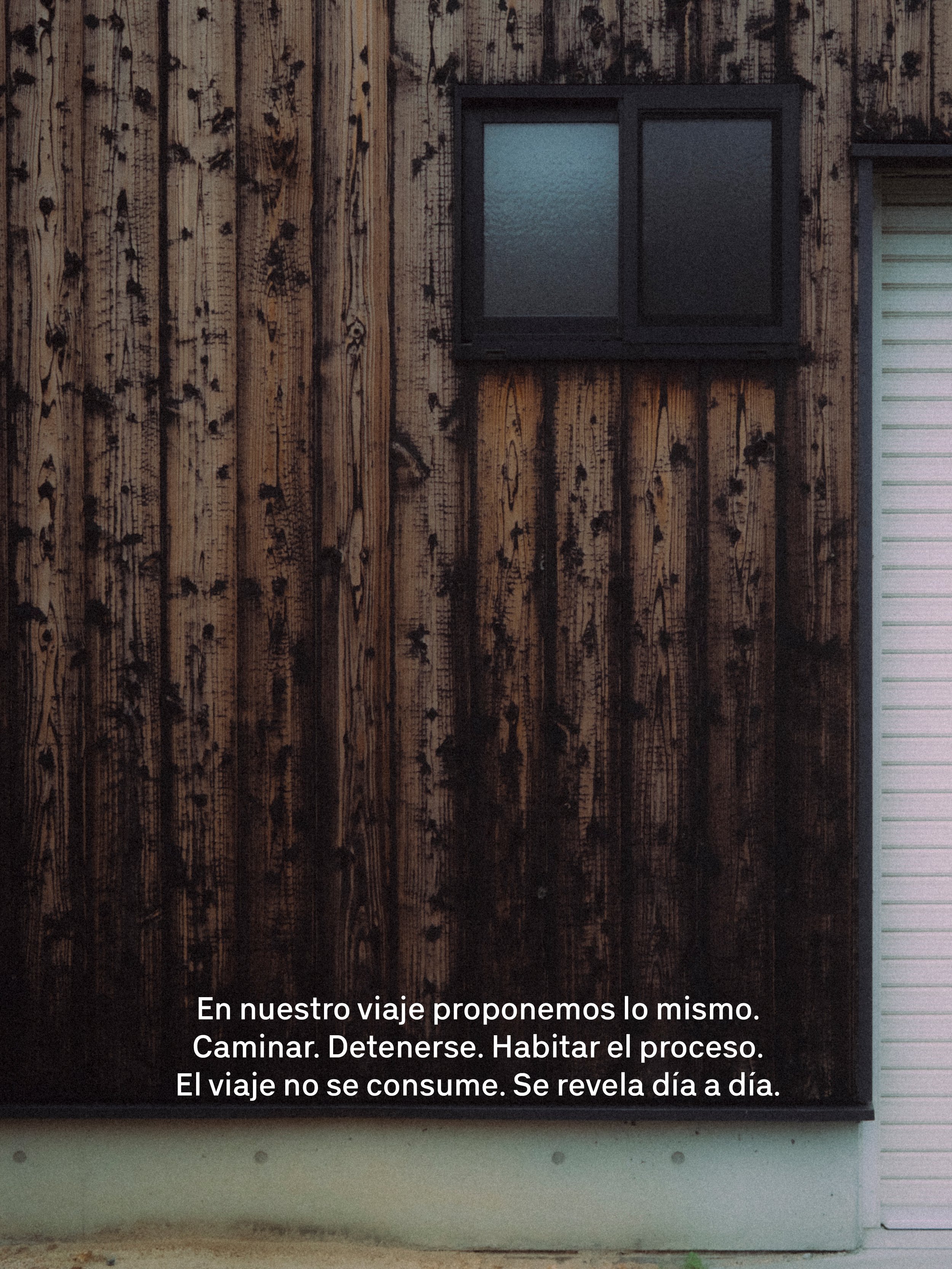 Texto en una pared de madera que dice: "En nuestro viaje proponemos lo mismo. Caminar. Detenerse. Habitar el proceso. El viaje no se consume. Se revela día a día."