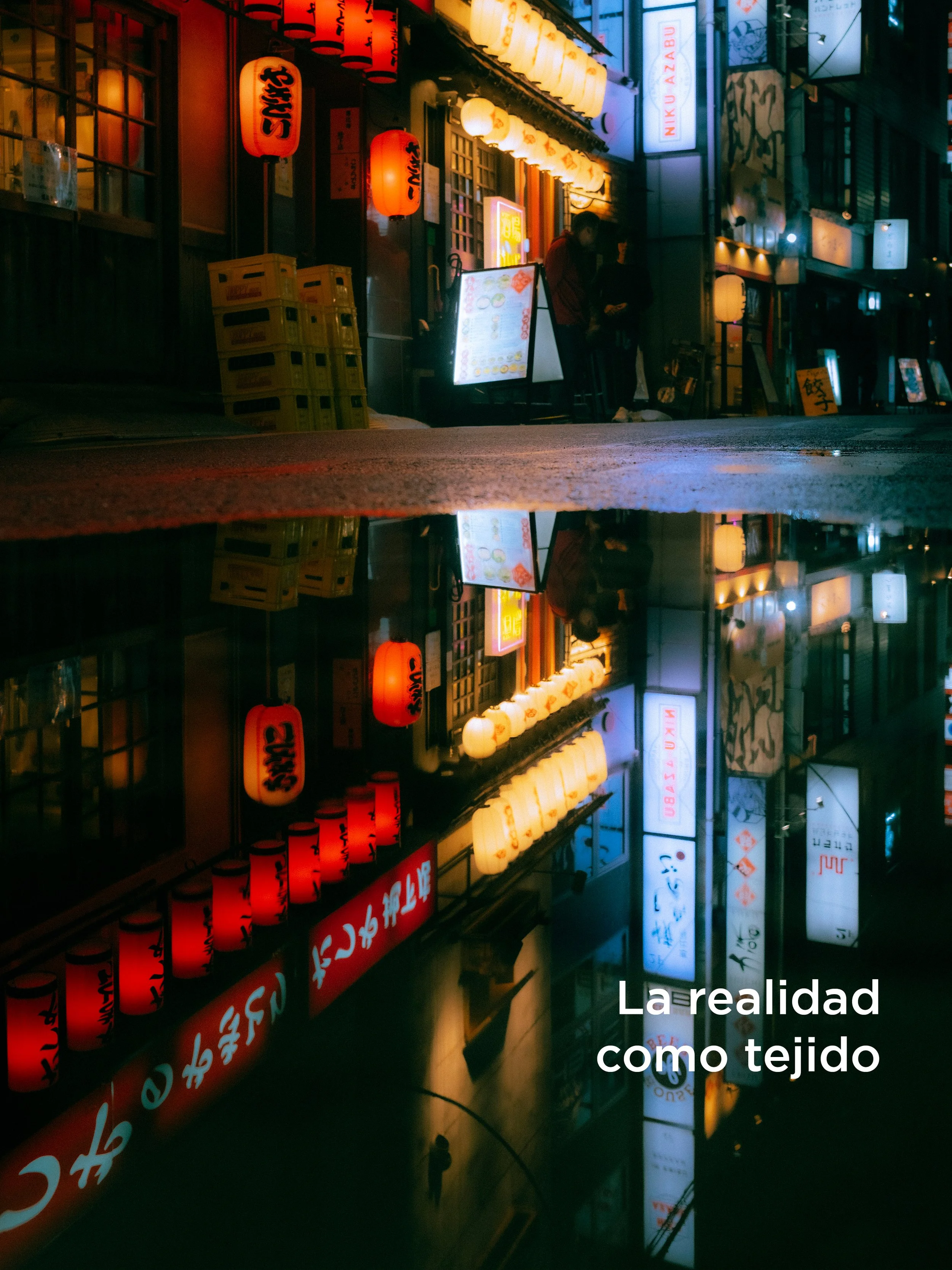 Caída de agua reflejada en el pavimento de una calle urbana, con letreros luminosos y linternas rojas y blancas en los edificios cercanos, sugiriendo una escena nocturna en Japón.