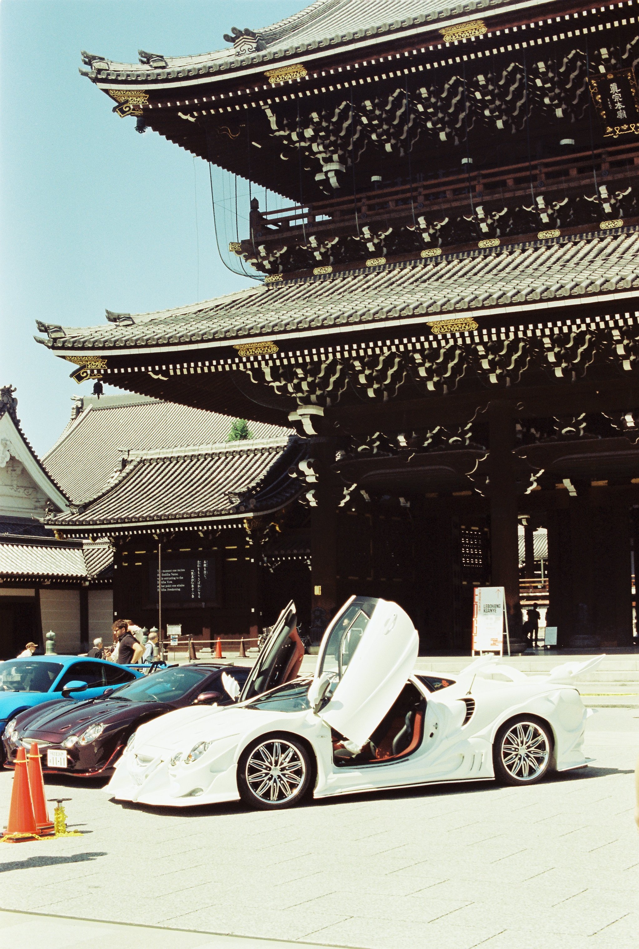 Carrera de autos deportivos de lujo en un evento frente a un templo tradicional japonés. Los autos son de colores blanco y negro y hay varias personas viendo el evento.