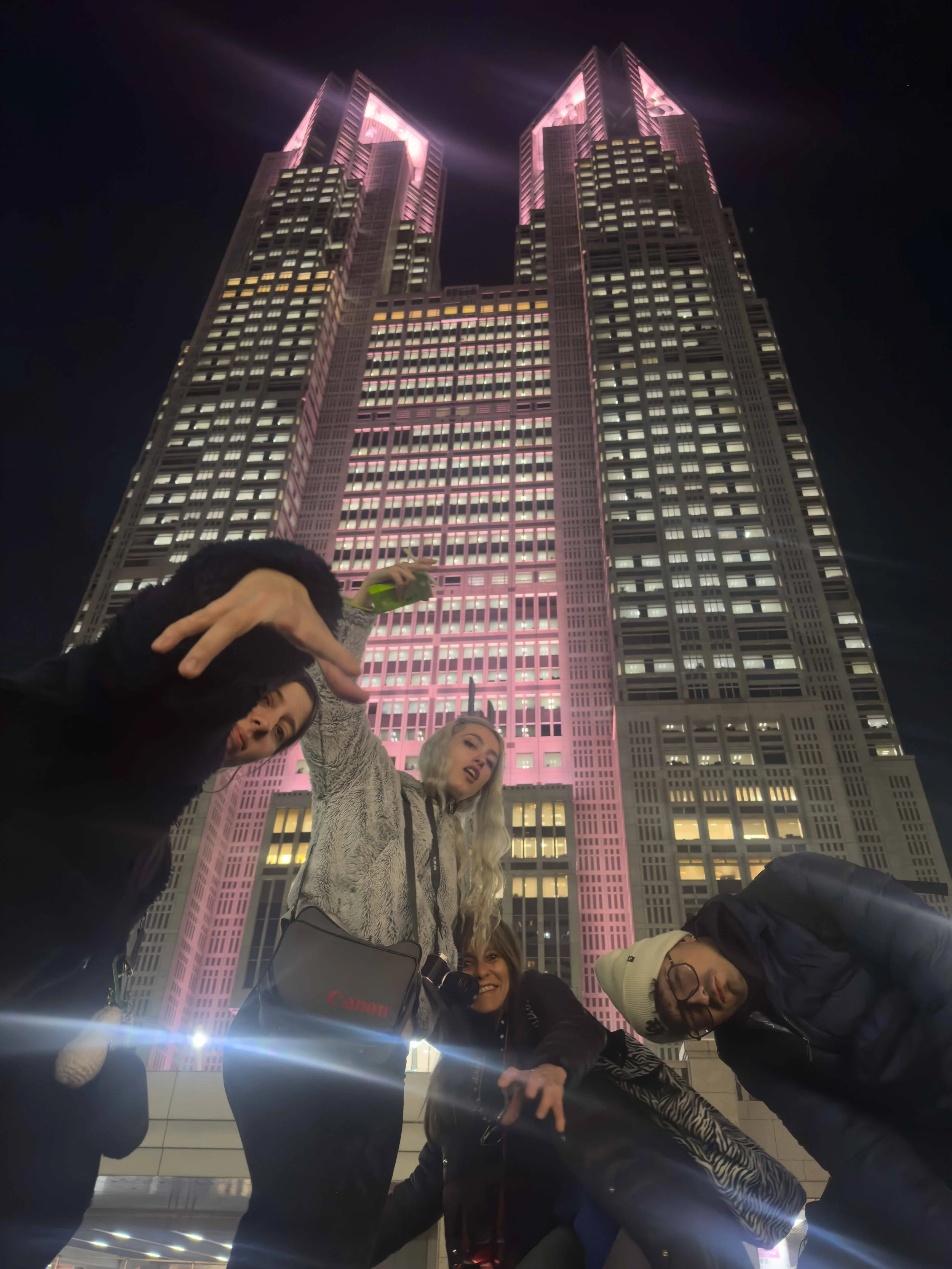Grupo de personas posando frente a un edificio iluminado de noche, algunas haciendo gestos y sonriendo.