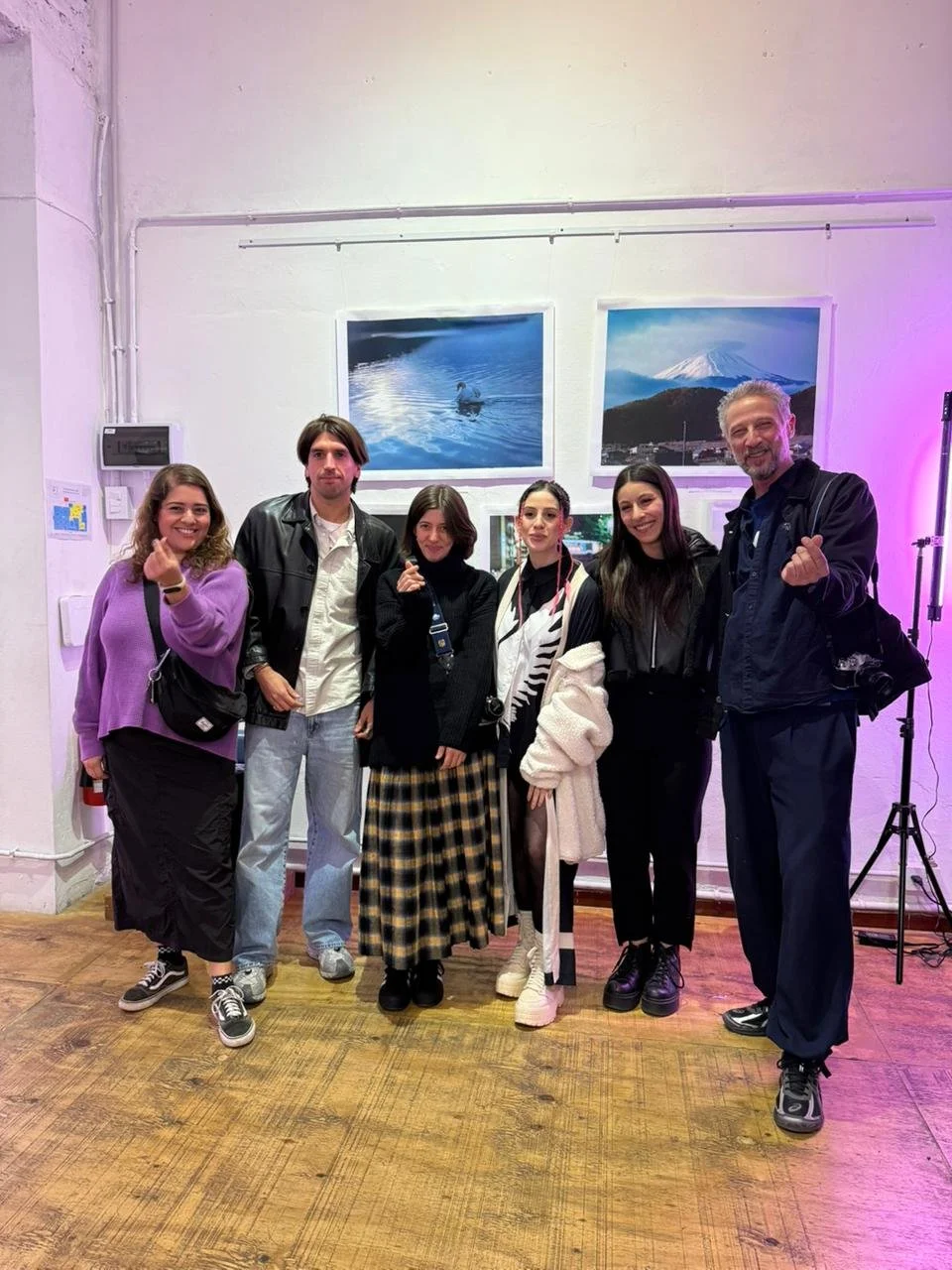 Grupo de seis personas posando en una galería de arte, con dos fotografías de paisajes en la pared detrás de ellos.