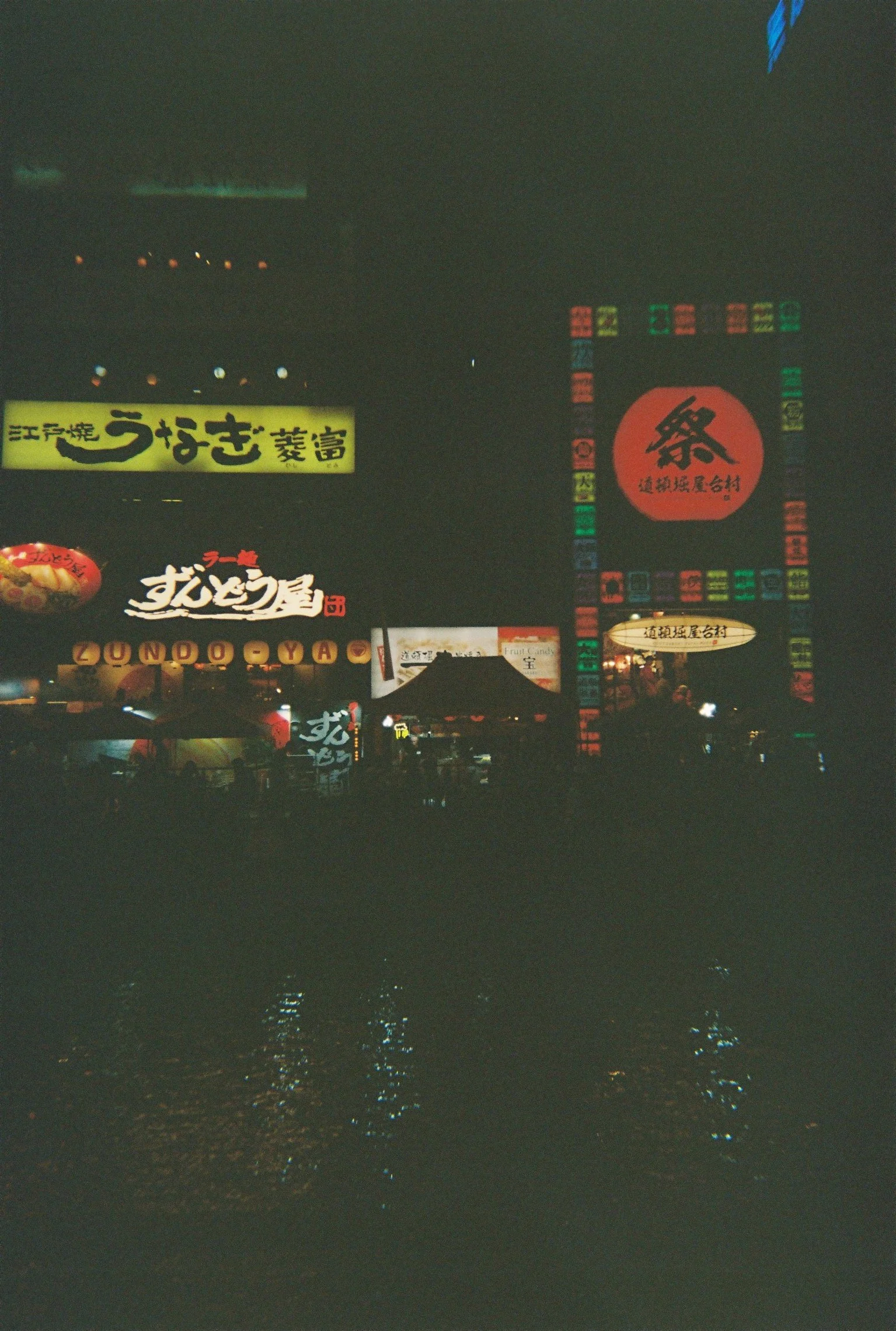 Vista nocturna de ciudades con letreros luminosos en japonés y reflejos en el agua.