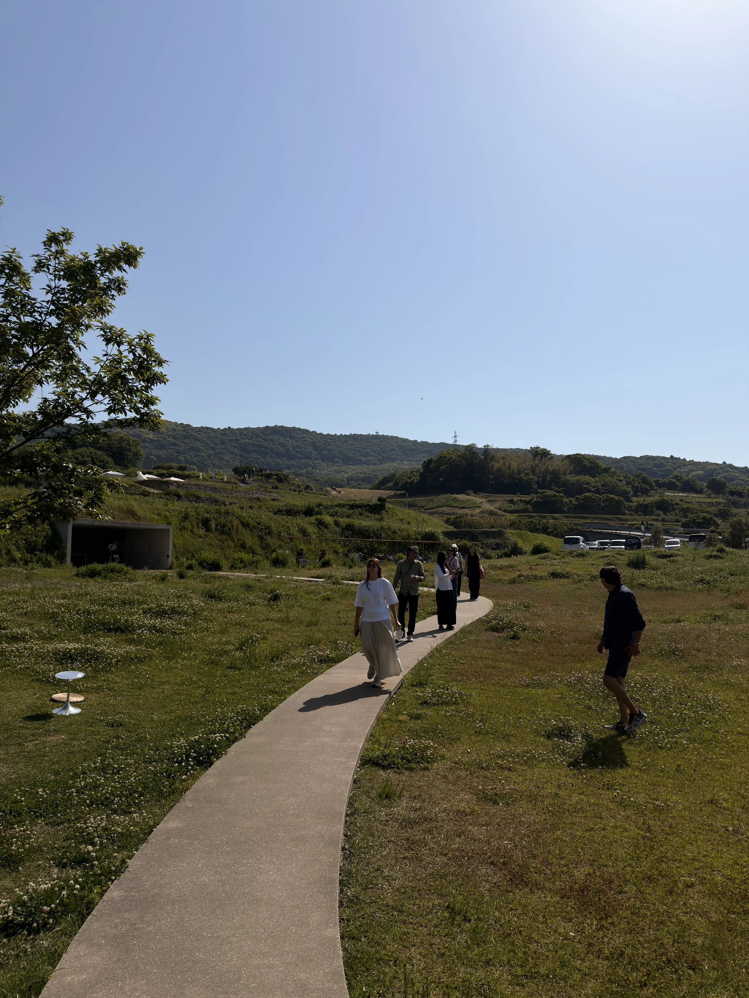 Personas caminando por un sendero en un parque con montañas y árboles en el fondo, en un día soleado y despejado.