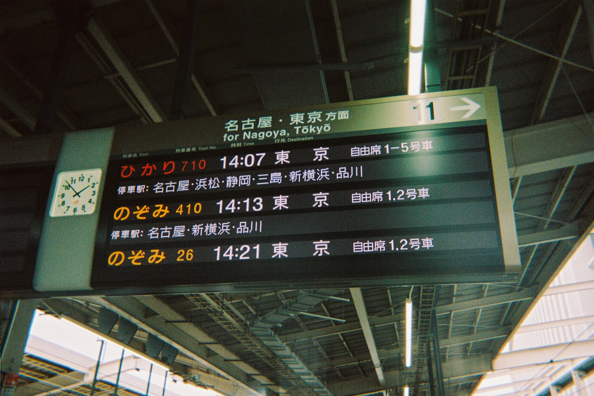 Pantalla de horario de tren en una estación, muestra trenes hacia Nagoya y Tokyo, con horarios y números de trenes en japonés.