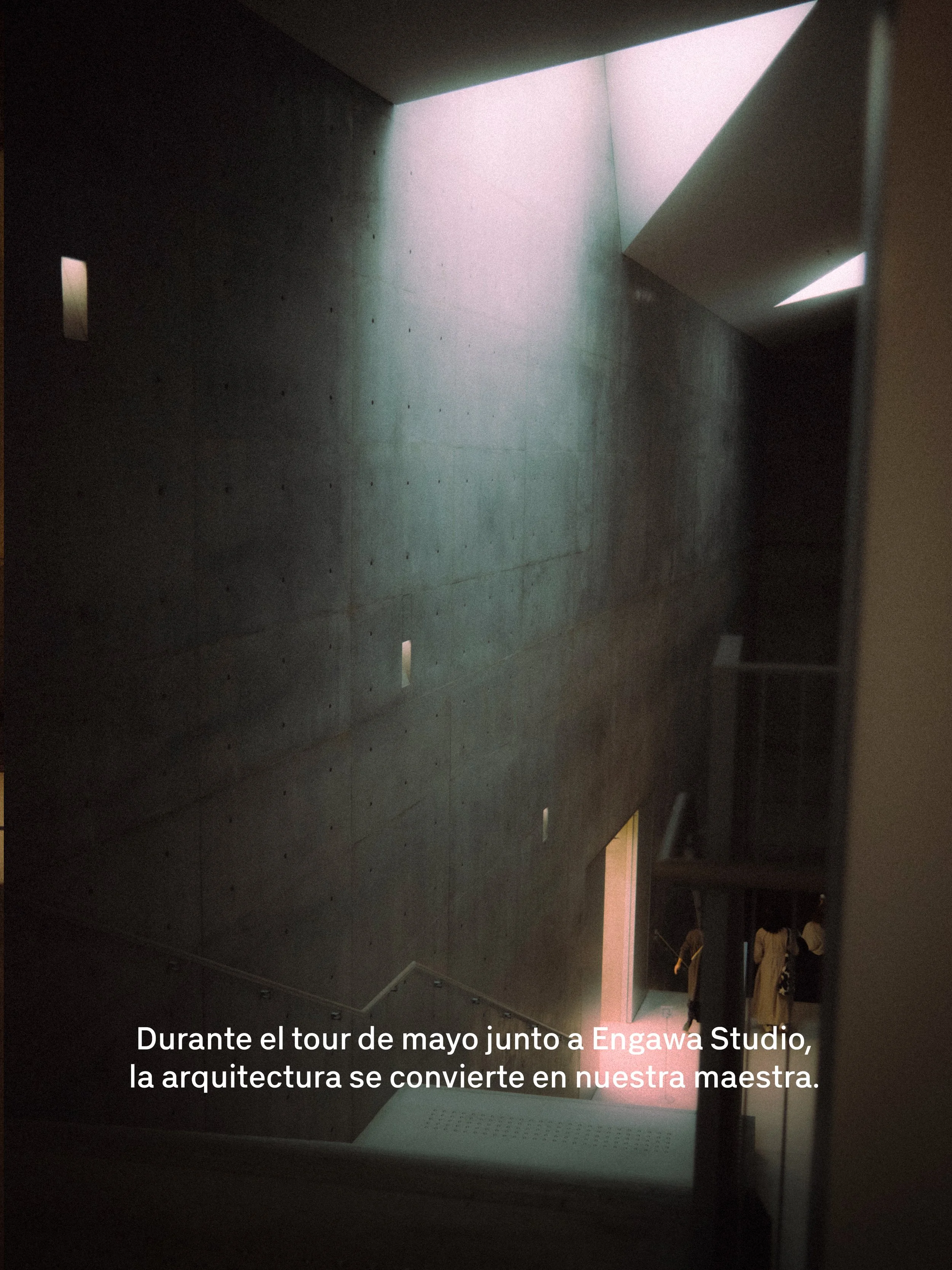 Interior de una arquitectura moderna con paredes de concreto y ventanas en la parte superior que permiten la entrada de luz natural. Se observa una escalera y una persona en la parte inferior derecha.