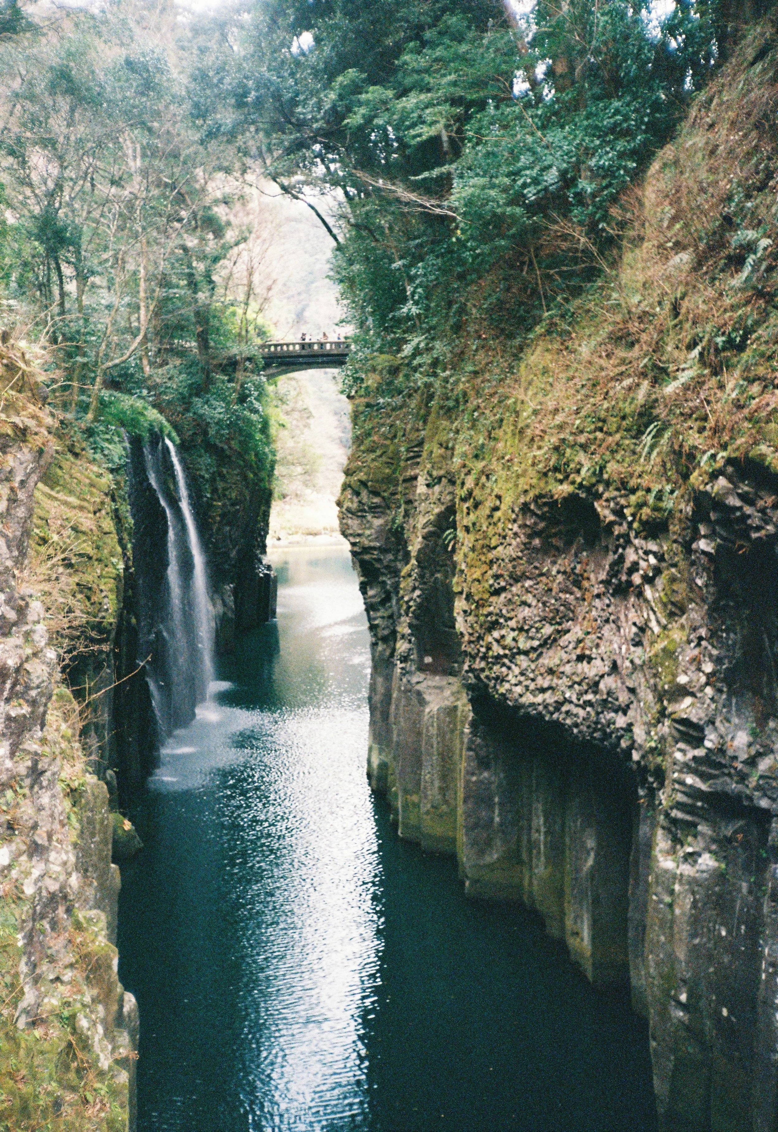 Cañón con cascada y puente en medio, rodeado de vegetación y rocas en el río.