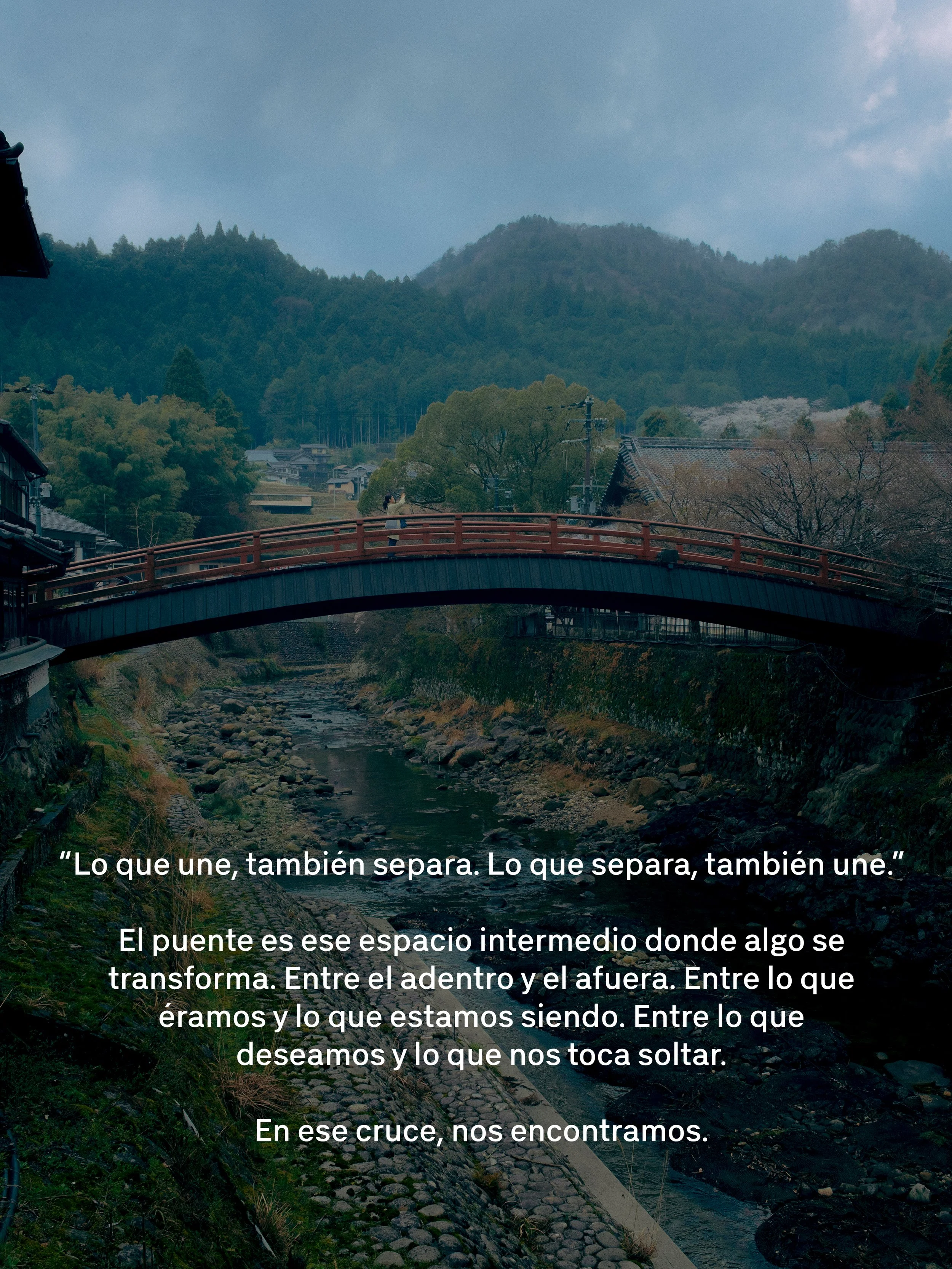 Un puente sobre un río rodeado de naturaleza con colinas y árboles, con una persona tomando una foto desde el puente.