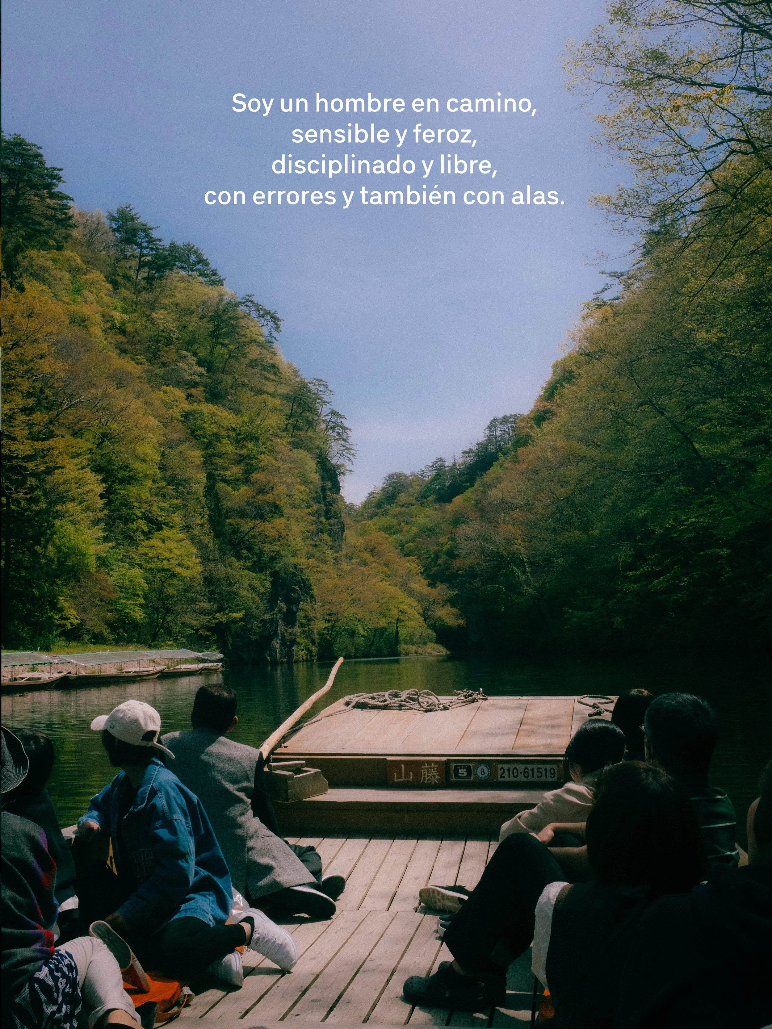 Grupo de personas en un bote de madera navegando por un río rodeado de bosques verdes y montañas, en un día soleado.