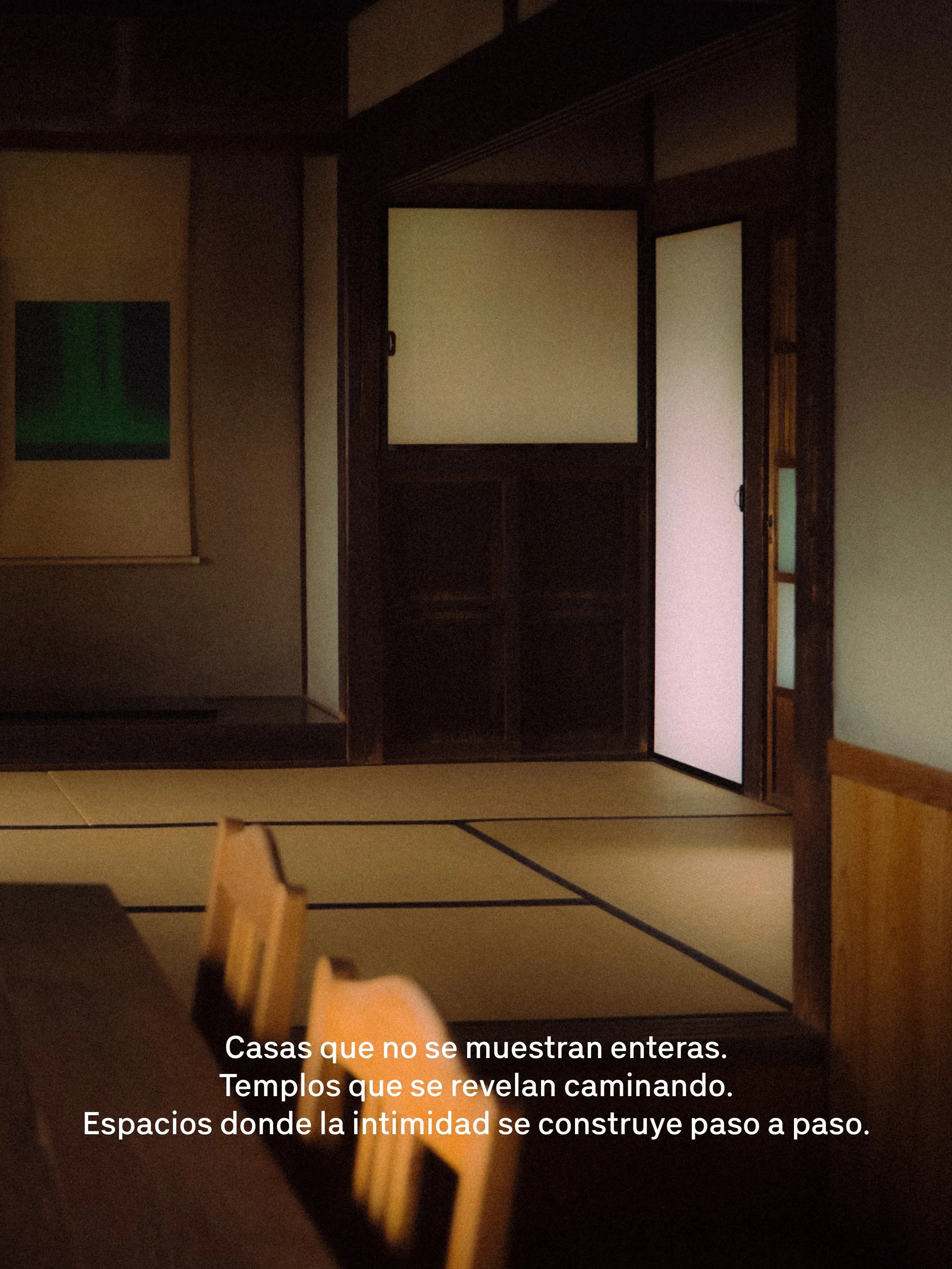 Imagen de interiores oscuros con puertas cerradas y una pintura en la pared. Se observa un ambiente reservado, con un par de sillas y una mesa en primer plano. Texto en la parte inferior que dice: "Casas que no se muestran enteras. Templos que se revelan caminando. Espacios donde la intimidad se construye paso a paso."