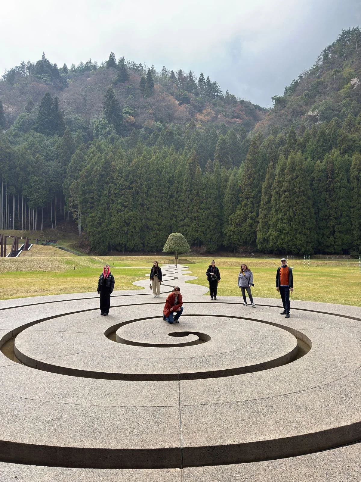 Grupo de personas posando en un monumento en forma de espiral en un parque rodeado de árboles y montañas