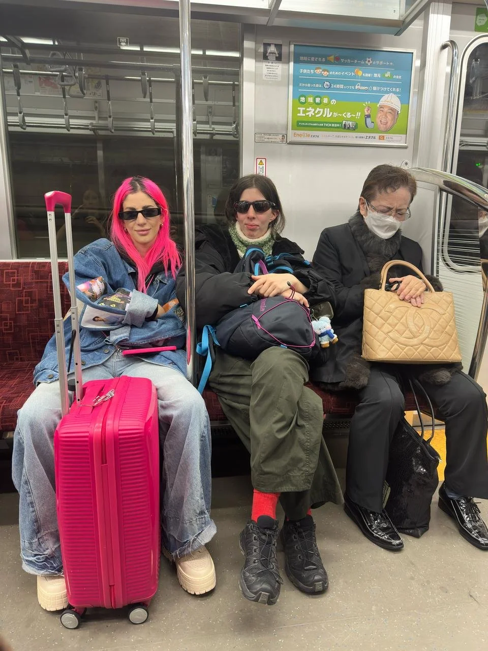 Tres personas sentadas en un vagón de tren, cada una con equipaje y usando gafas o mascarilla.