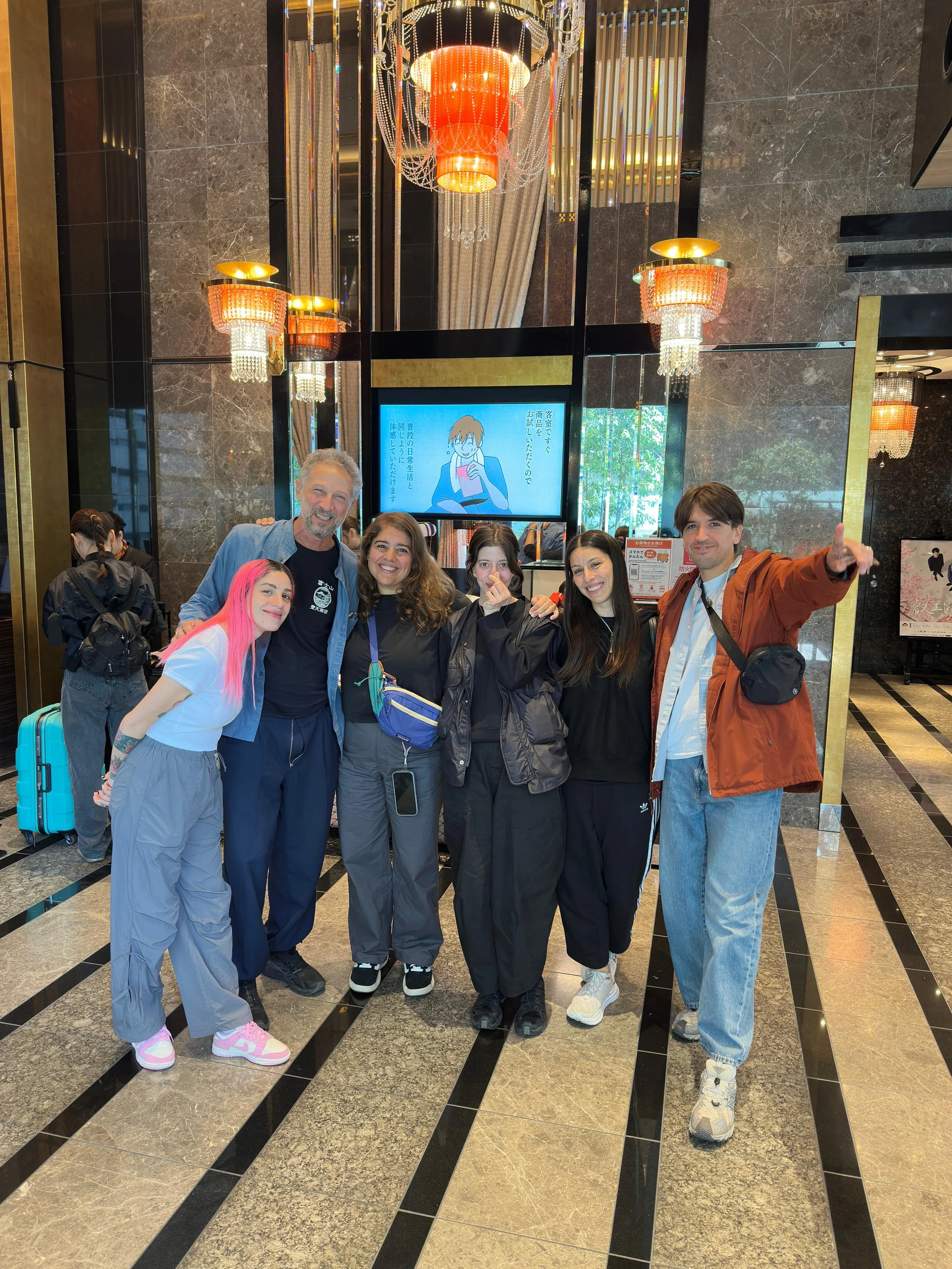 Grupo de seis personas posando y sonriendo en un vestíbulo de hotel elegante con paredes de mármol oscuro, con un gran panel de pantalla y candelabros decorativos en el fondo.