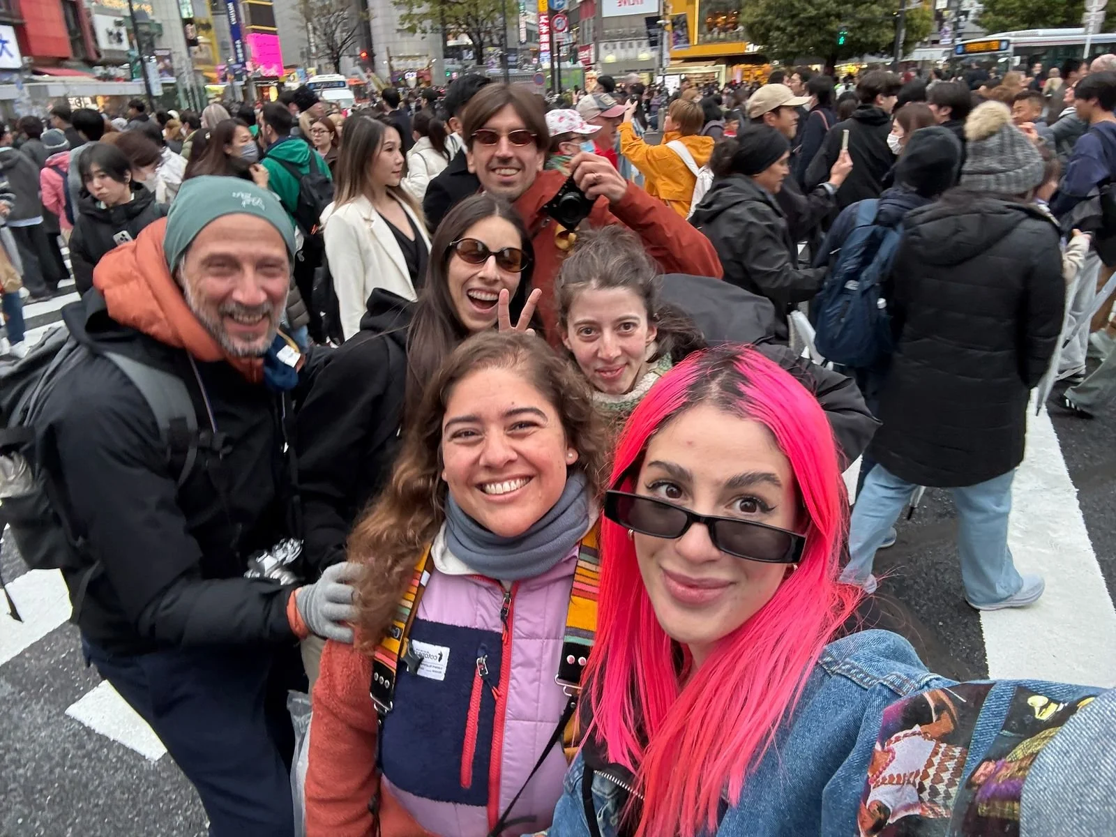 Grupo de personas sonrientes y posando para una selfie en la calle en medio de una multitud, en un lugar urbano concurrido.