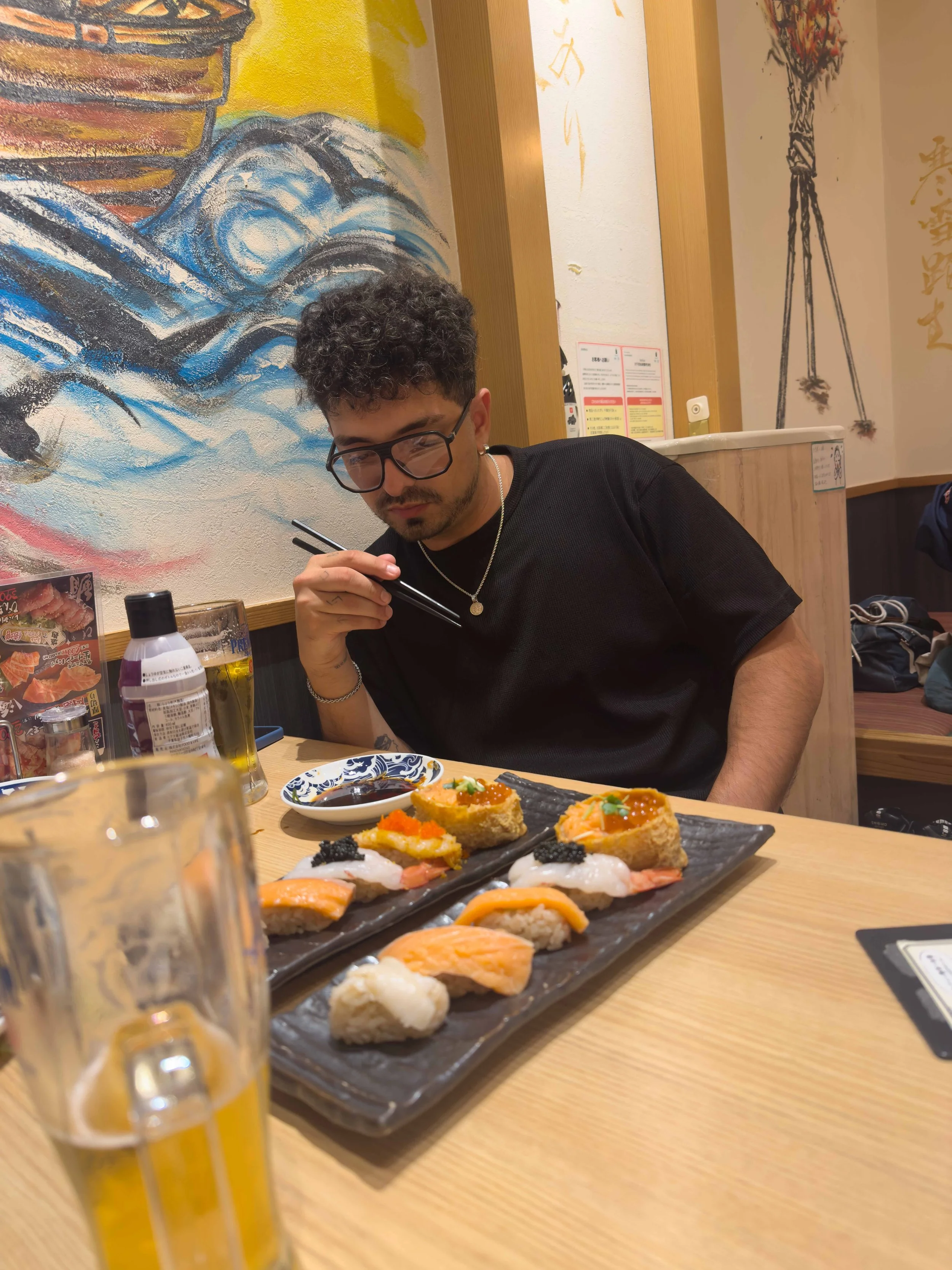 Joven con barba y gafas comiendo sushi en un restaurante japonés.