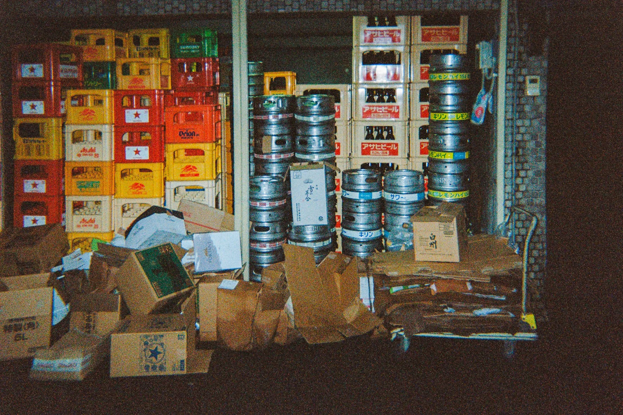Estantería con cajas, cervezas enlatadas y botellas, rodeada de cajas de cartón en un espacio de almacenamiento.
