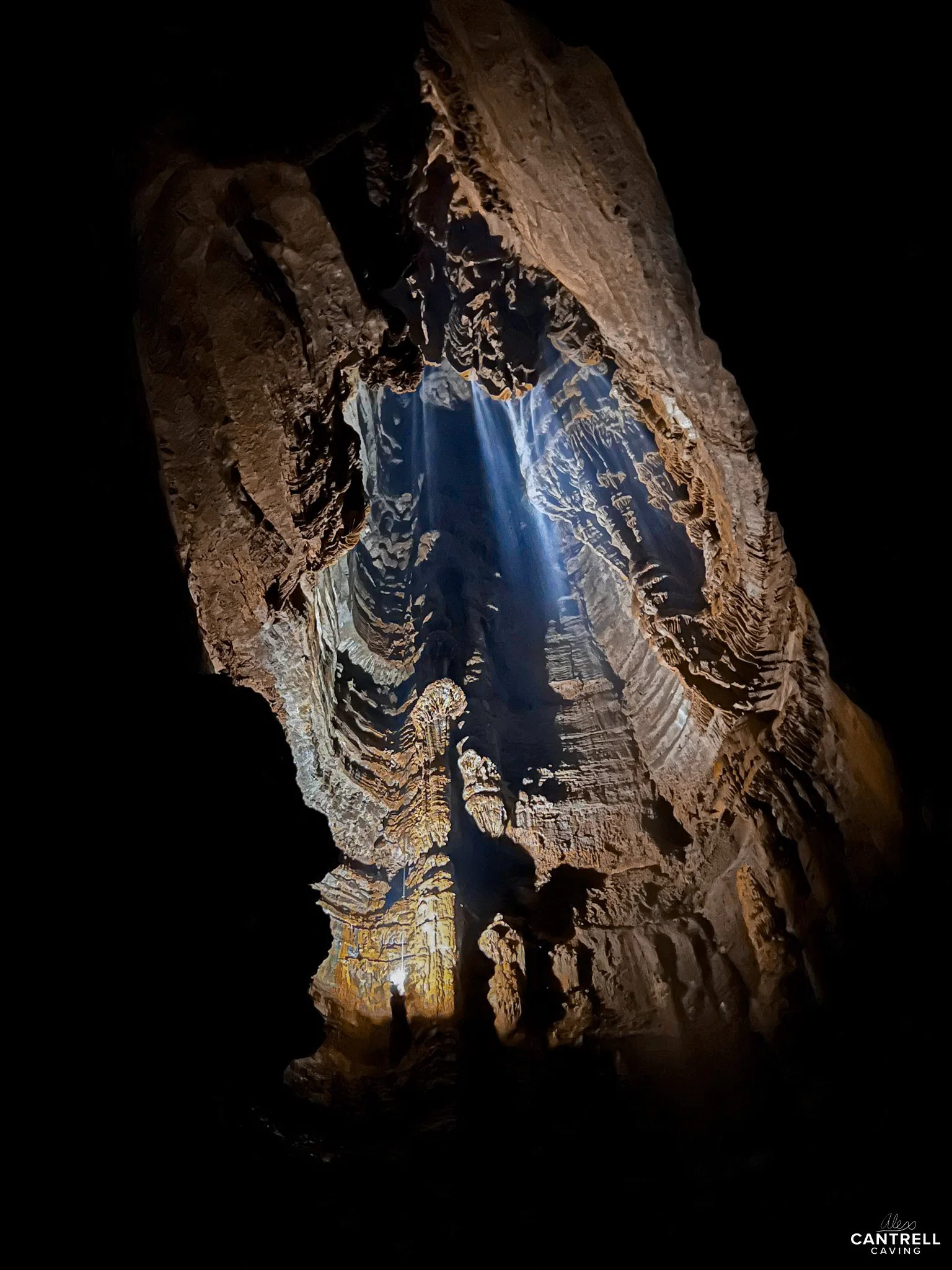Rays of sunlight entering a dark cave, illuminating the rough, textured rock formations inside. The cave walls are jagged and layered, creating an intricate natural pattern.
