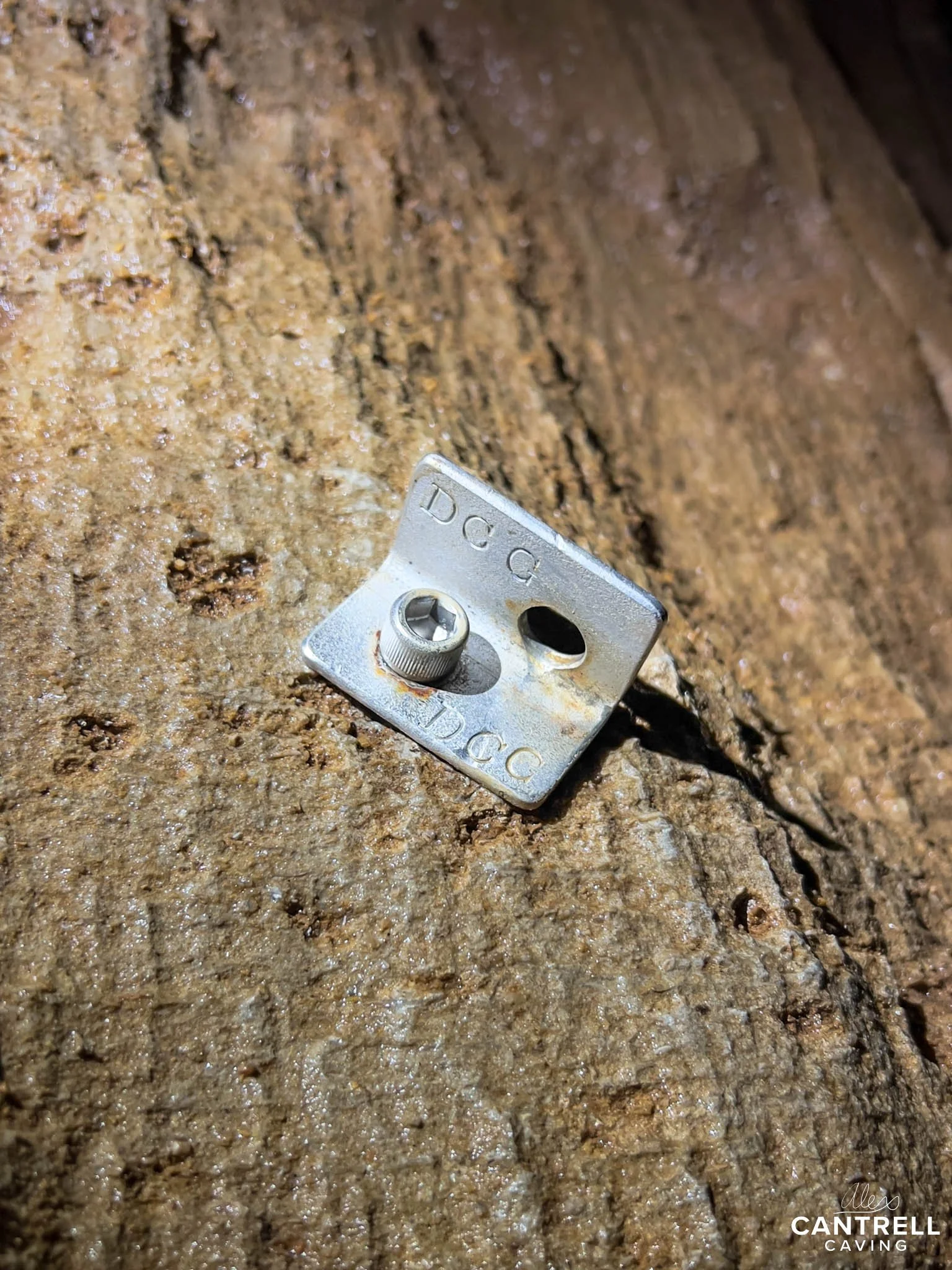 Rock climbing bolt anchor secured in a cave wall with visible metal bolt and plate.