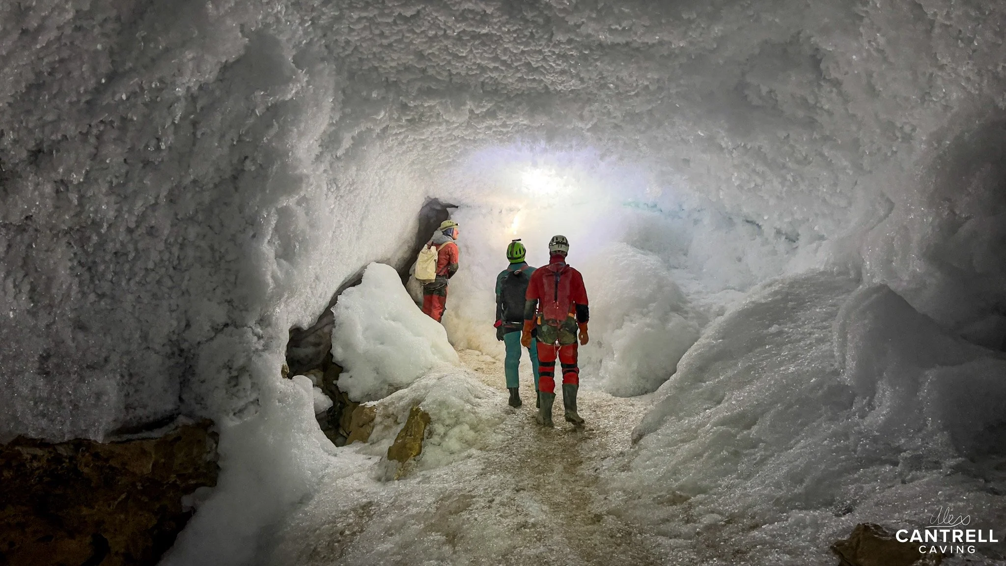 Cavers exploring an icy cave with ice formations and wearing protective gear.