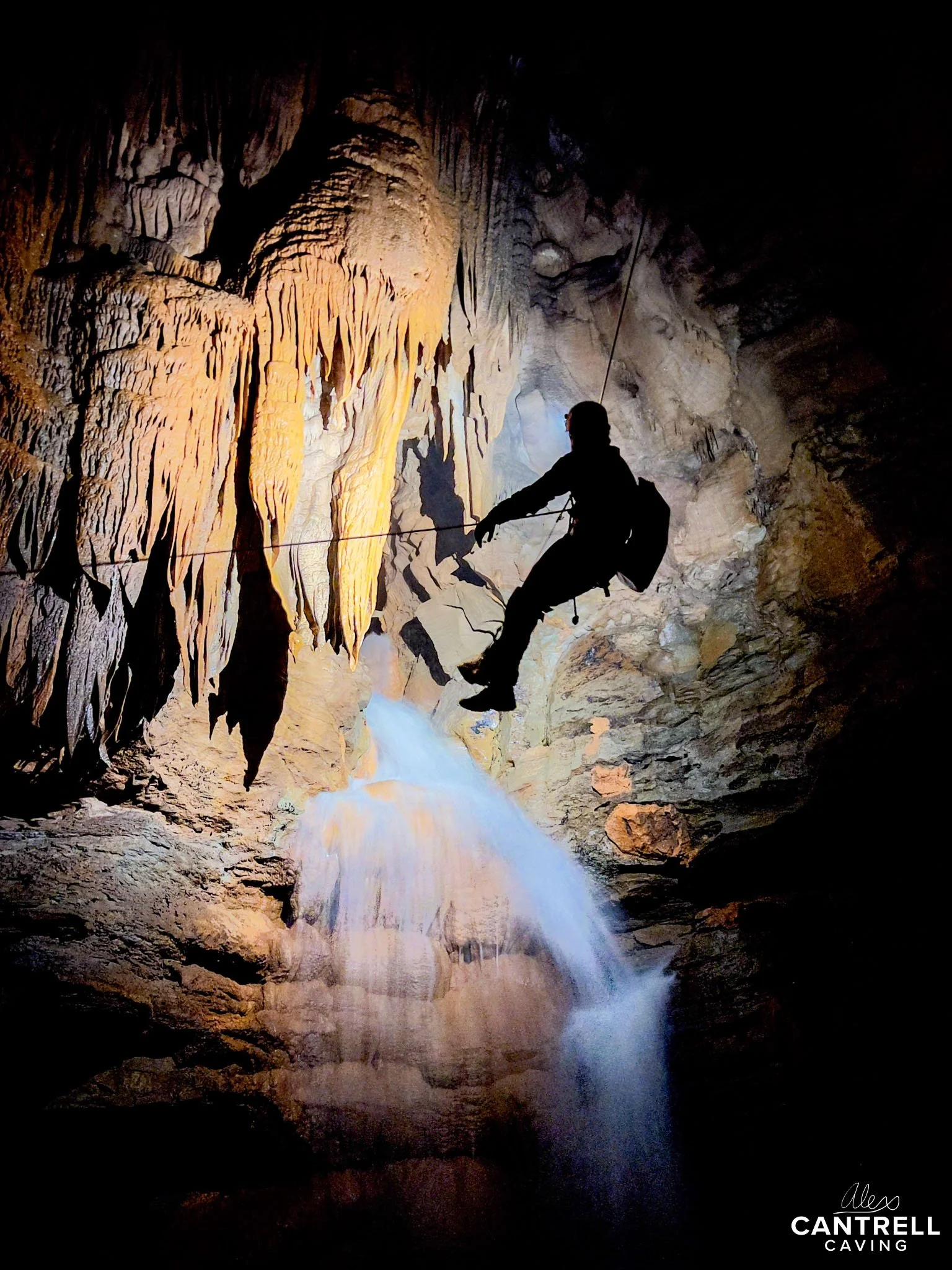 Silhouette of a person rappelling in a cave near a waterfall