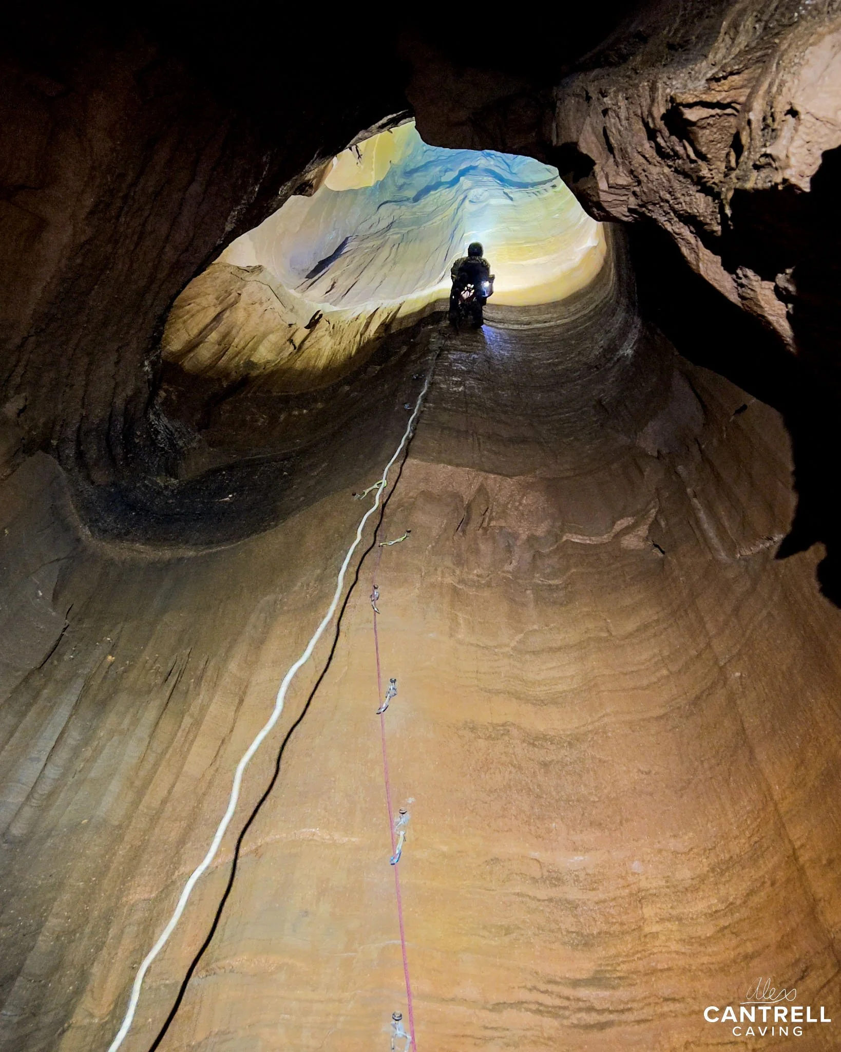 Person ascending inside a large cave with ropes and climbing gear.