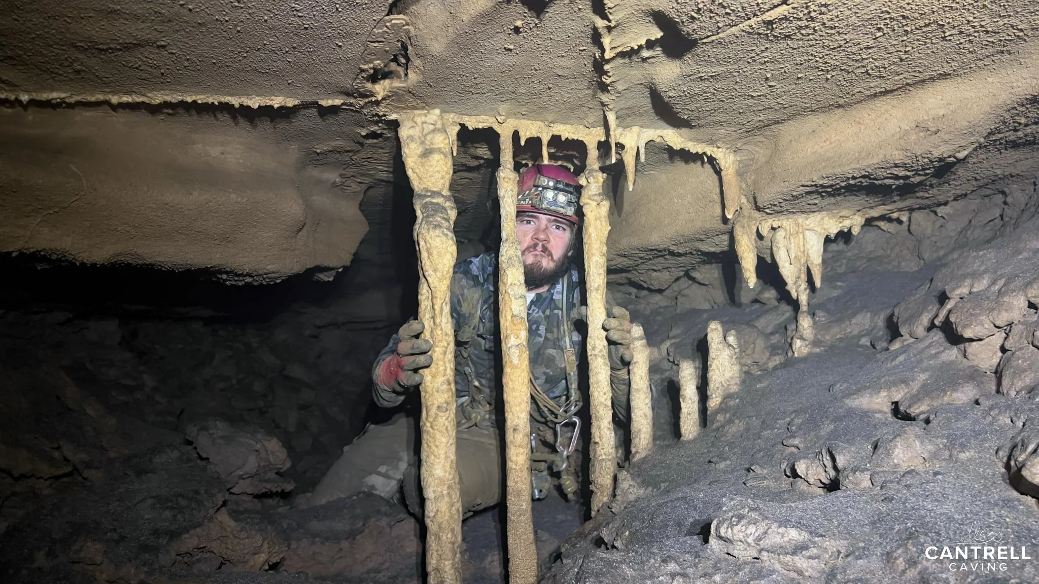 Cave explorer navigating tight passage with stalactites.