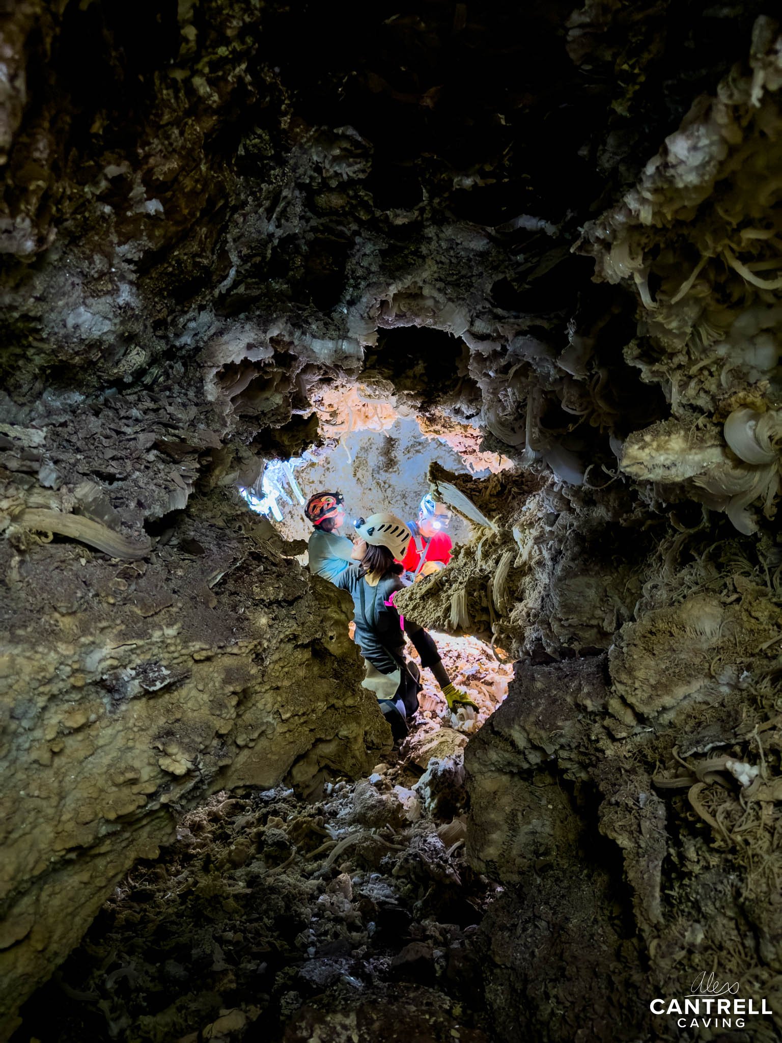 Caver exploring a rocky cave passage, wearing a helmet and headlamp.