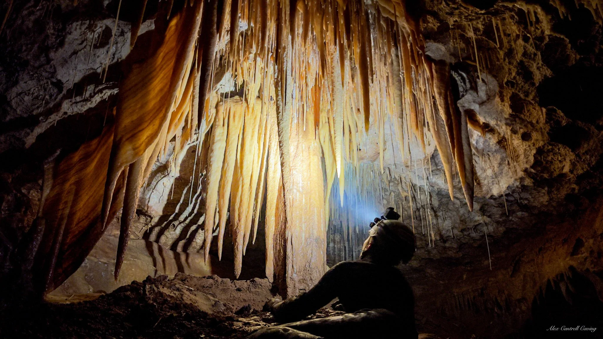 Person exploring a cave with stalactites and a flashlight
