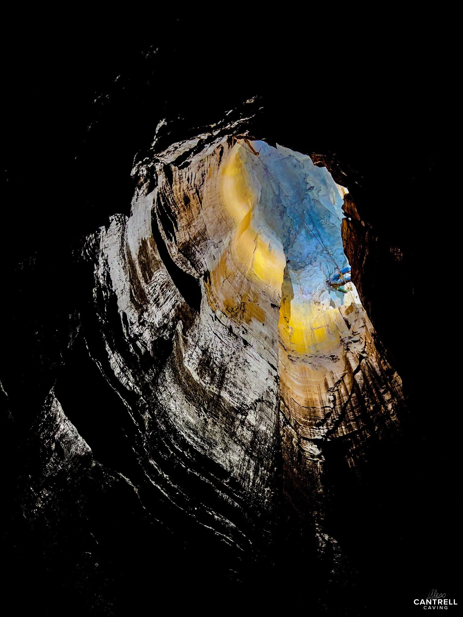 View looking up from inside a cave or cavern, showcasing textured rock walls with natural light illuminating the central area in shades of yellow and blue.