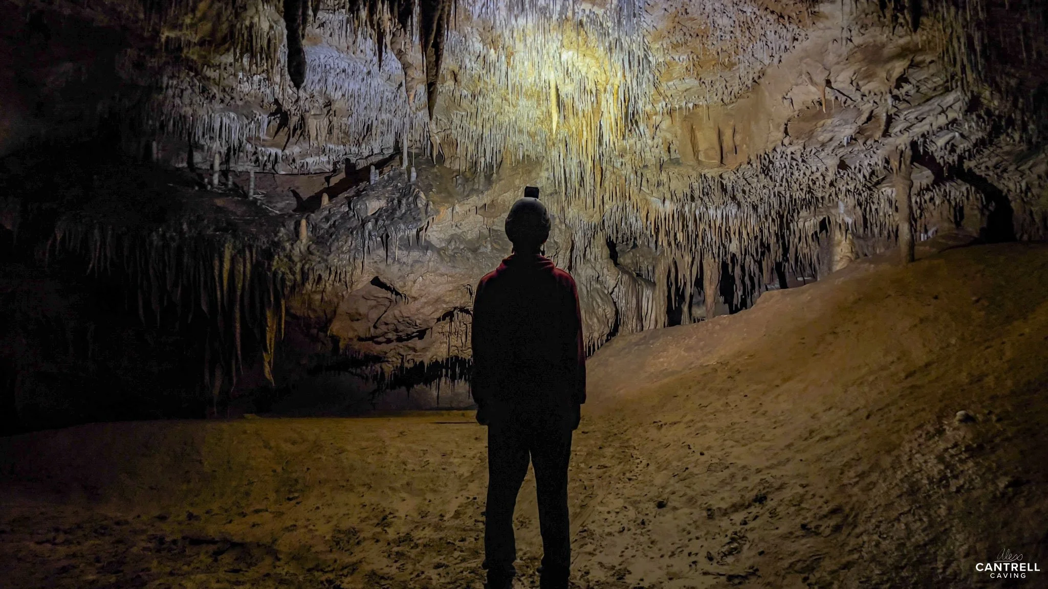 Person standing inside a cave with stalactites and stalagmites.