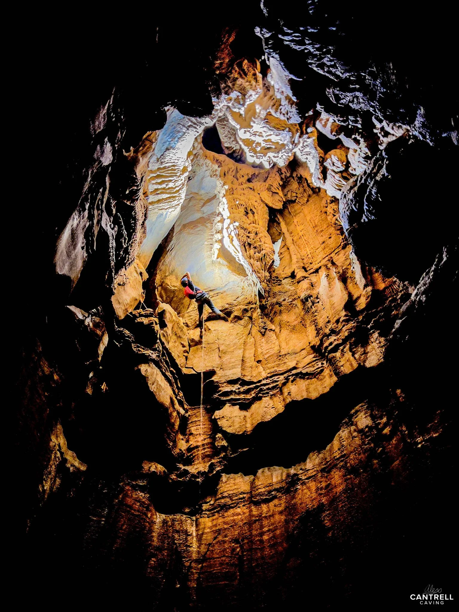 Person rappelling inside a large, illuminated cave with textured rock walls.