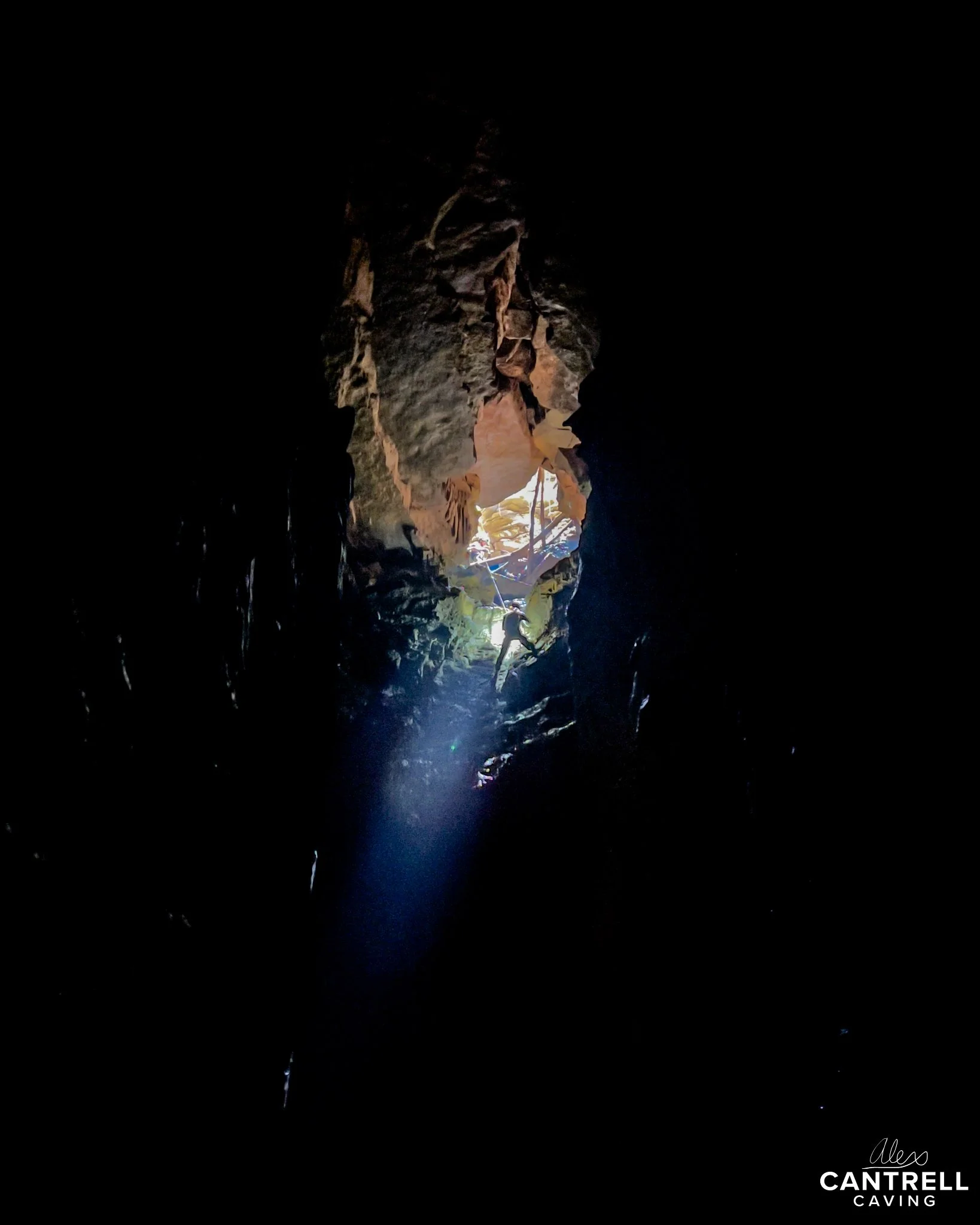 A dark cave interior with a beam of light illuminating a rock formation. The cave is mostly dark with some visible textures and formations on the walls.