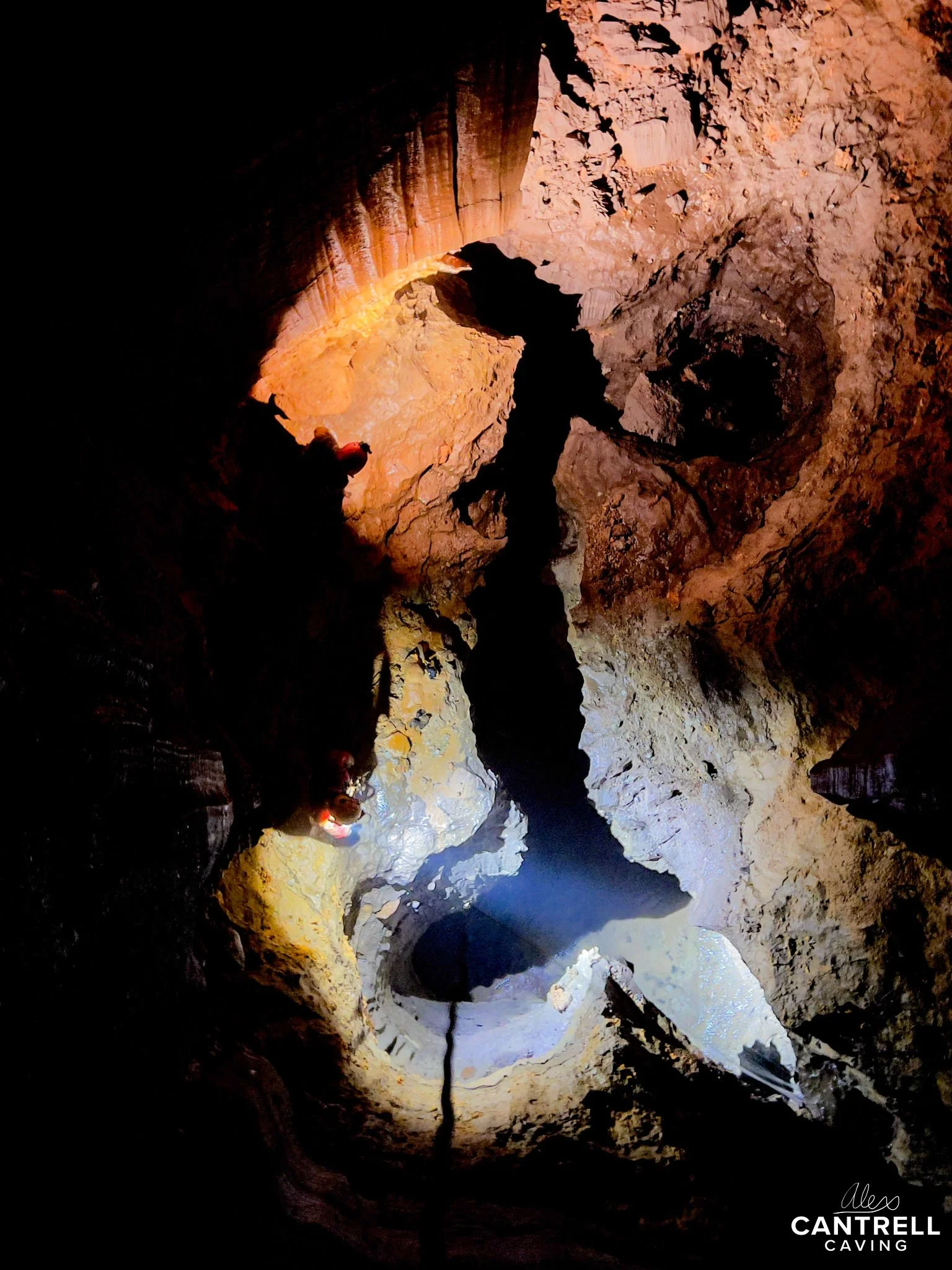 Cave interior with rock formations and cavers exploring.