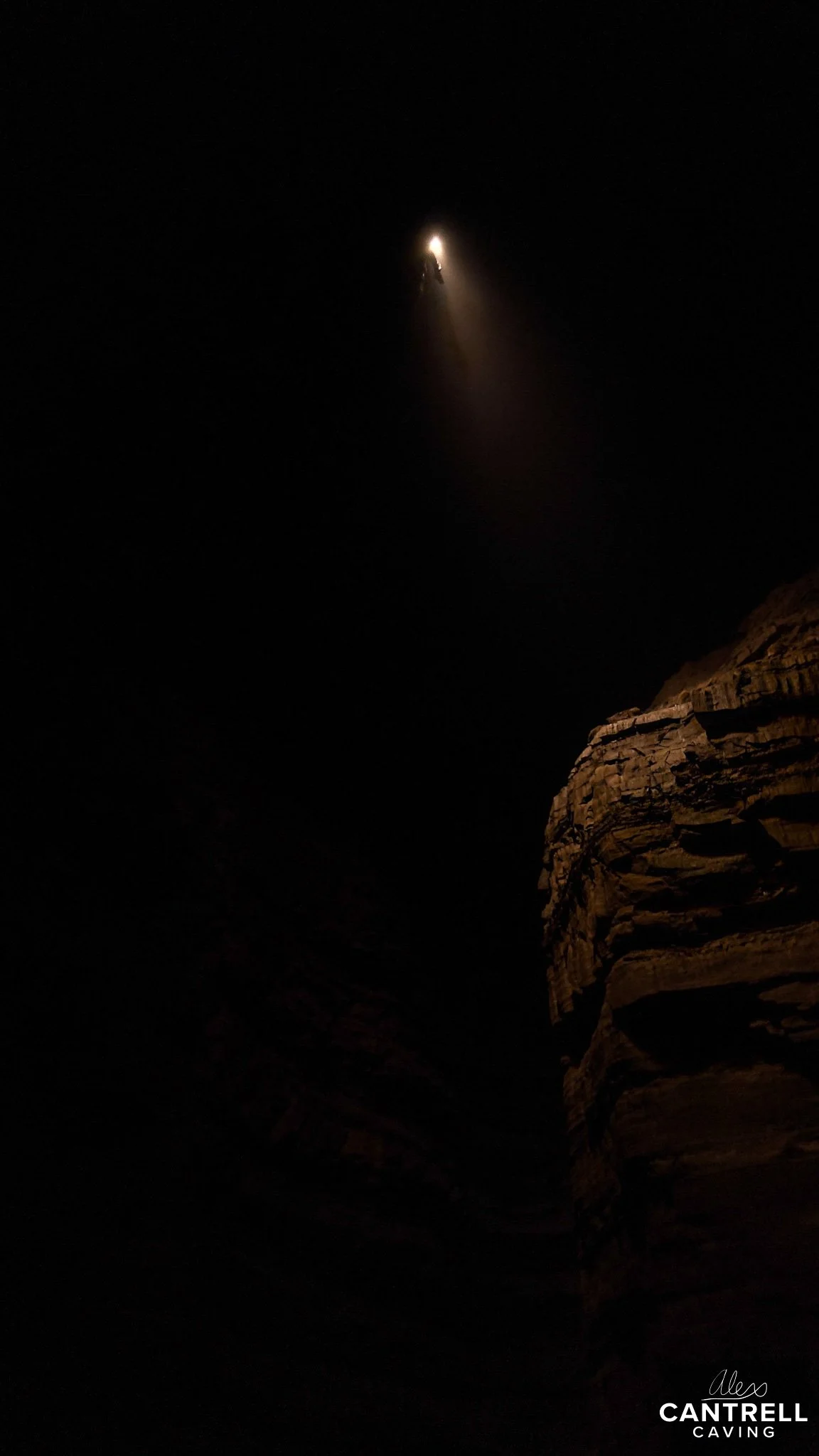 Interior of a dark cave with a climber illuminated by light from above, rocky walls visible.